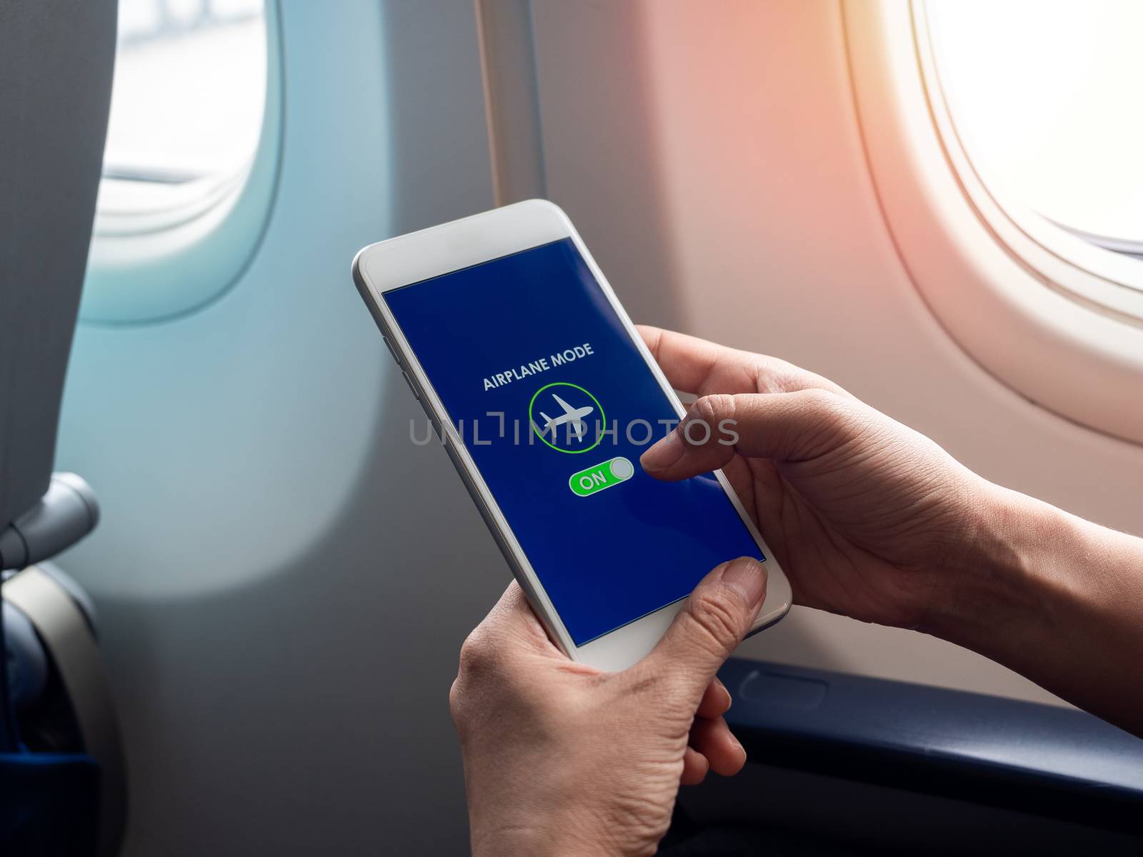 Flight mode concept. Finger sliding on screen for turned on airplane mode near the window on the airplane.