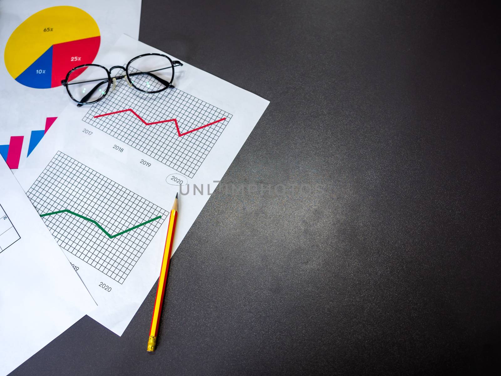 Business goal concept. Top view of business accessory, diagrams graphs, pencil and glasses on dark table with copy space.