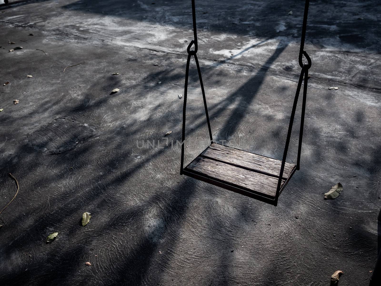 Old lonely wooden swing on sunset time with light and shadow. Vintage wood swing with leaves on the ground with copy space.