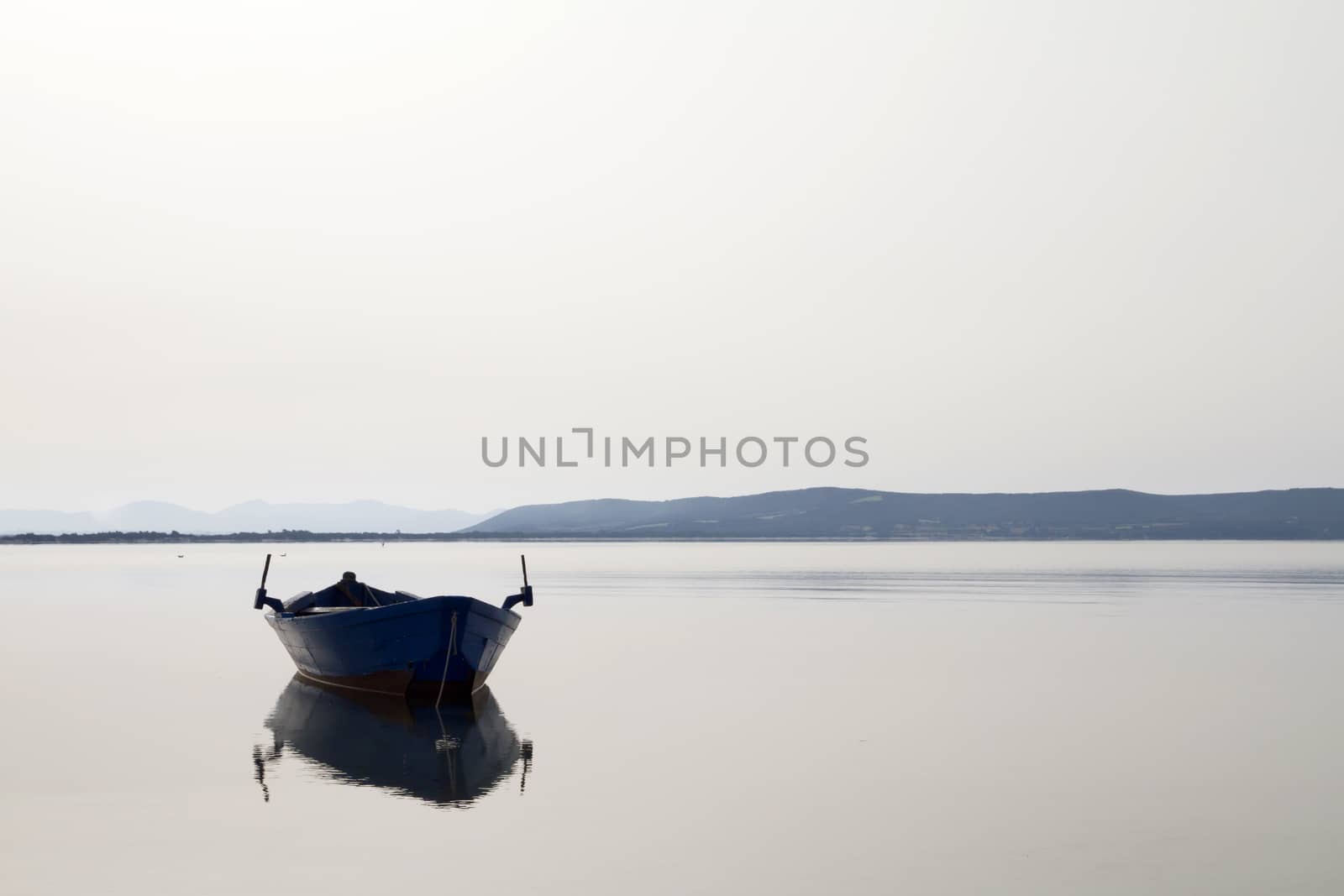 Fishing boat anchored in a sea bay with flat water that merges with the white sky