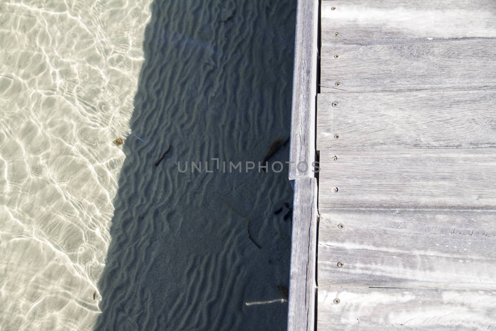 Wooden boardwalk on transparent sea water with sand on bottom. Geometric composition with shadows play.