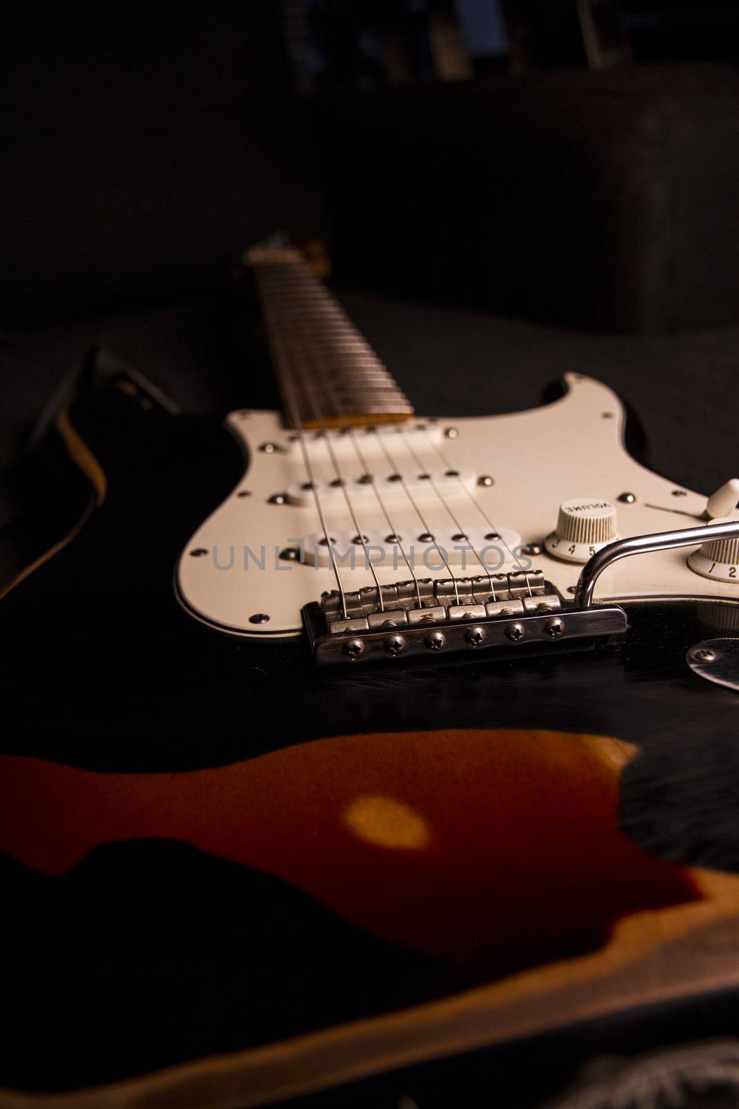 Close-up of a sunburst-colored electric guitar covered with black paint removed at certain points to create the worn out effect