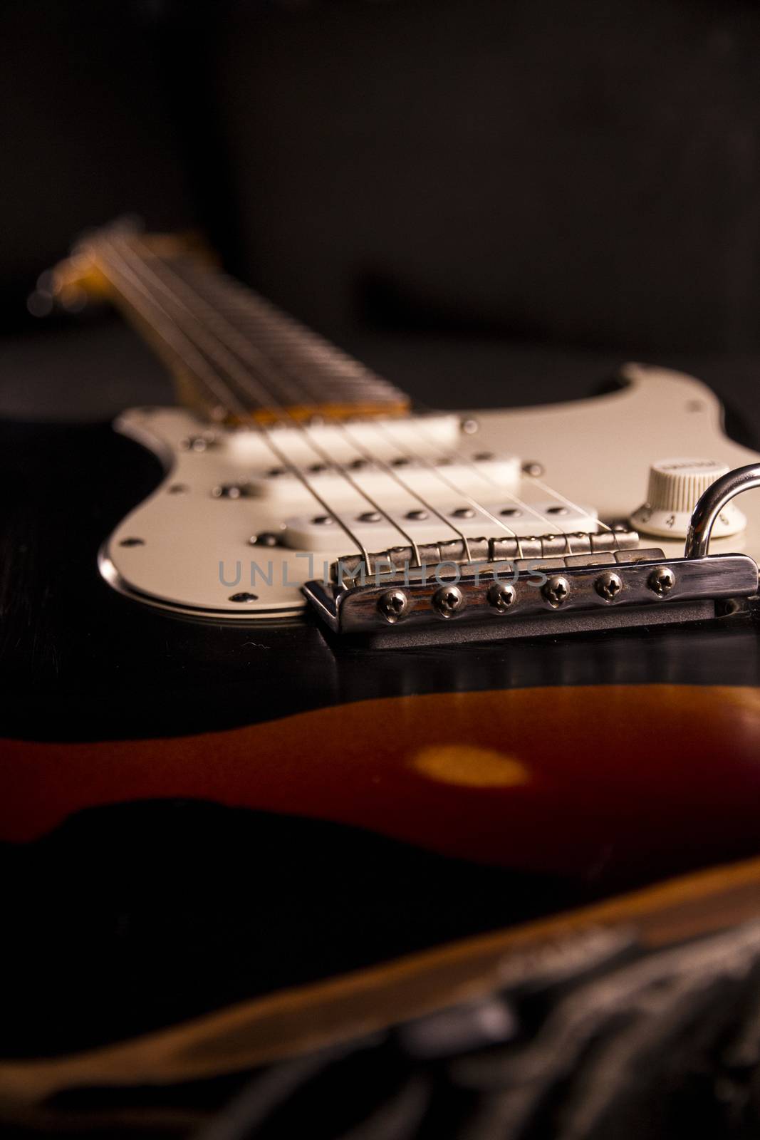 Close-up of a sunburst-colored electric guitar covered with black paint removed at certain points to create the worn out effect