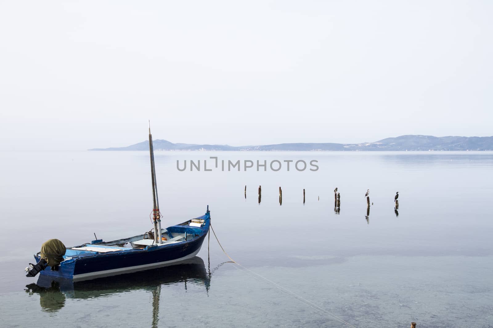 Fishing boat anchored in a sea bay with flat water that merges w by robbyfontanesi