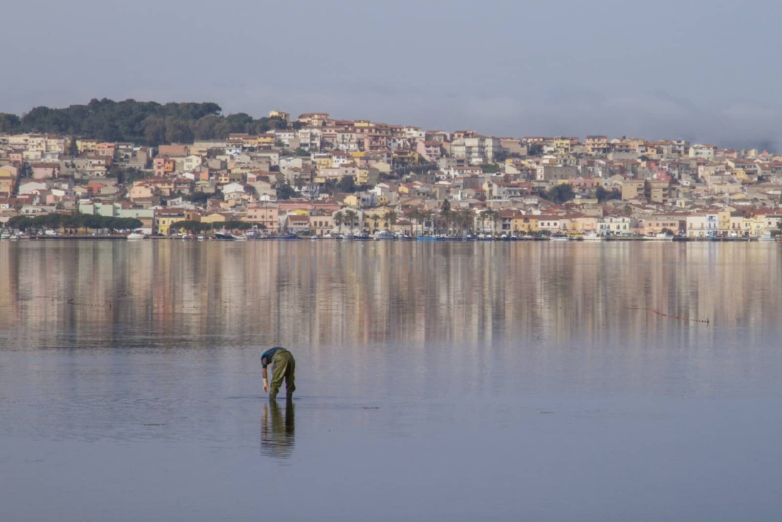 A fisherman at work bending in the flat sea water that reflects  by robbyfontanesi