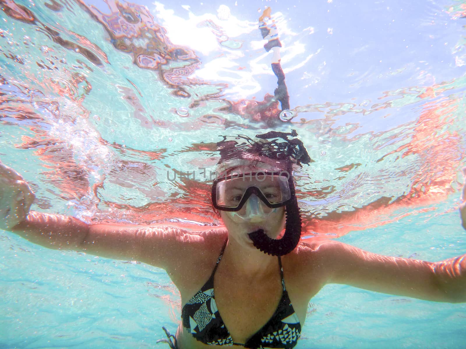 Young woman shooting in water from below with open arms with mask and snorkel in a beautiful game of colored water reflections