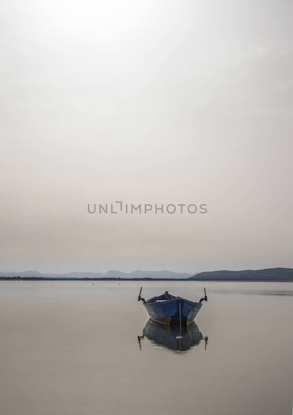 Fishing boat anchored in a sea bay with flat water that merges w by robbyfontanesi