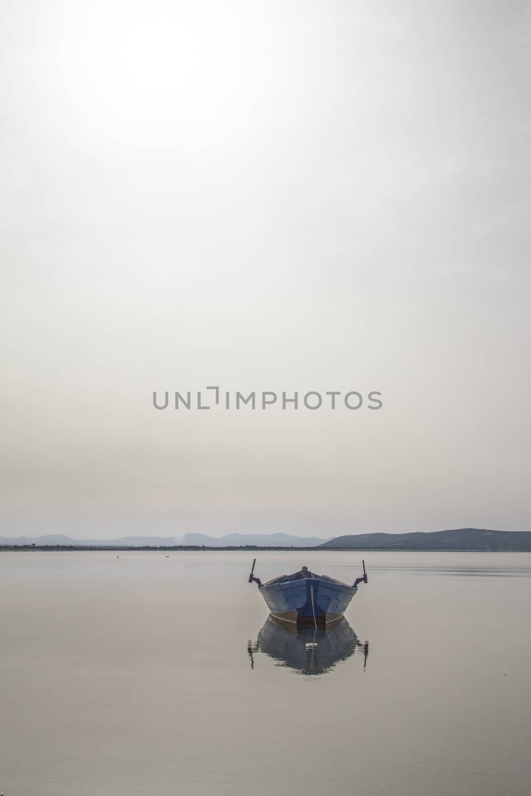 Fishing boat anchored in a sea bay with flat water that merges w by robbyfontanesi