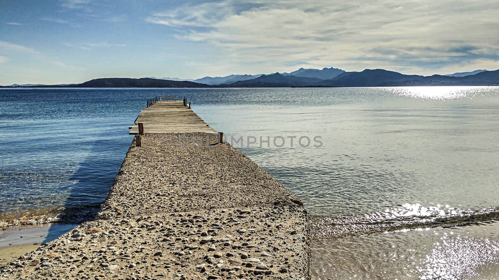 An old little pier proceeds for a few meters on the calm waters of the island of Tavolara in the colors of the Sardinian sea