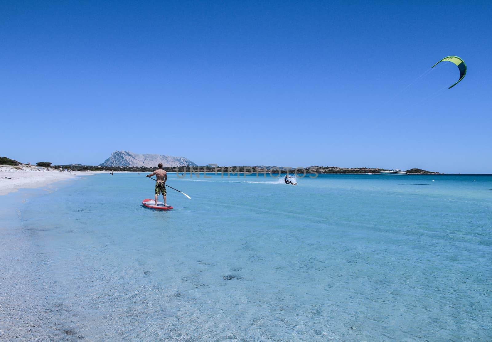 San Teodoro - La Cinta Beach - 2017 July - A young athlete paddle on stand up paddle on the crystalline sea of Sardinia, while a kitesurfer slides on the water beside him