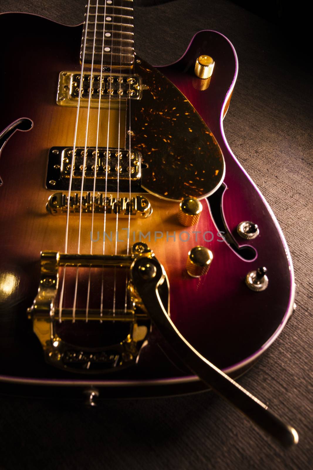 Closeup of sunburst electric guitar with brass mechanics and bright colors on a dark shaded background