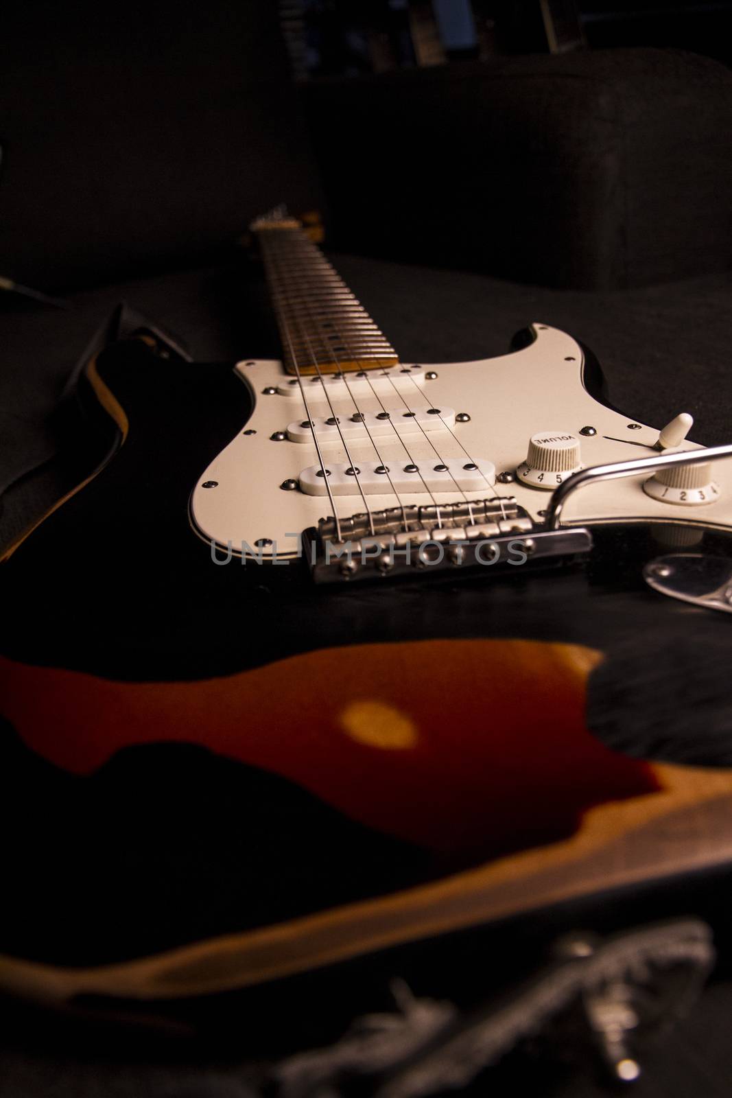 Close-up of a sunburst-colored electric guitar covered with black paint removed at certain points to create the worn out effect