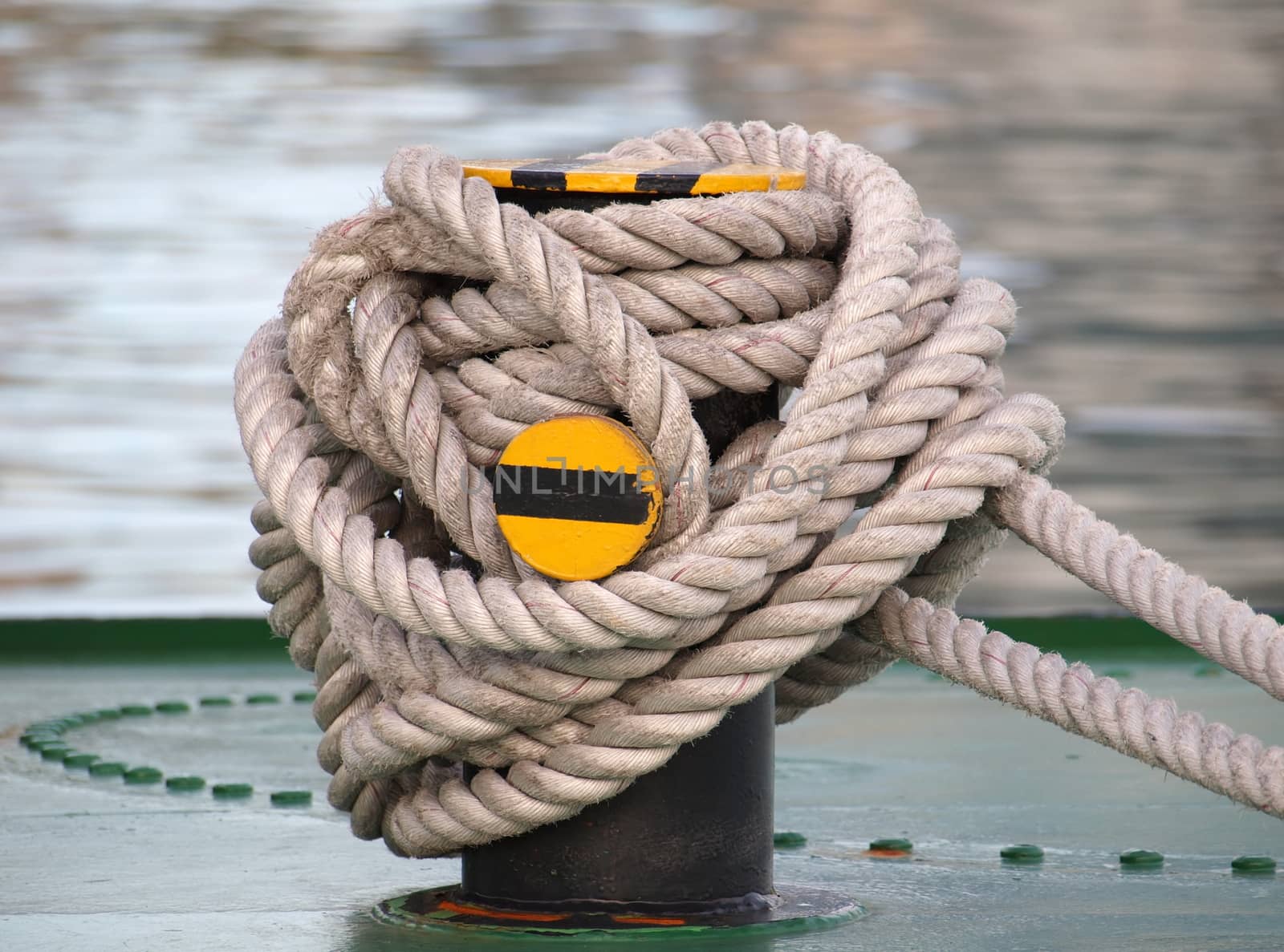 A thick rope is wrapped around a strong post on deck of a ship
