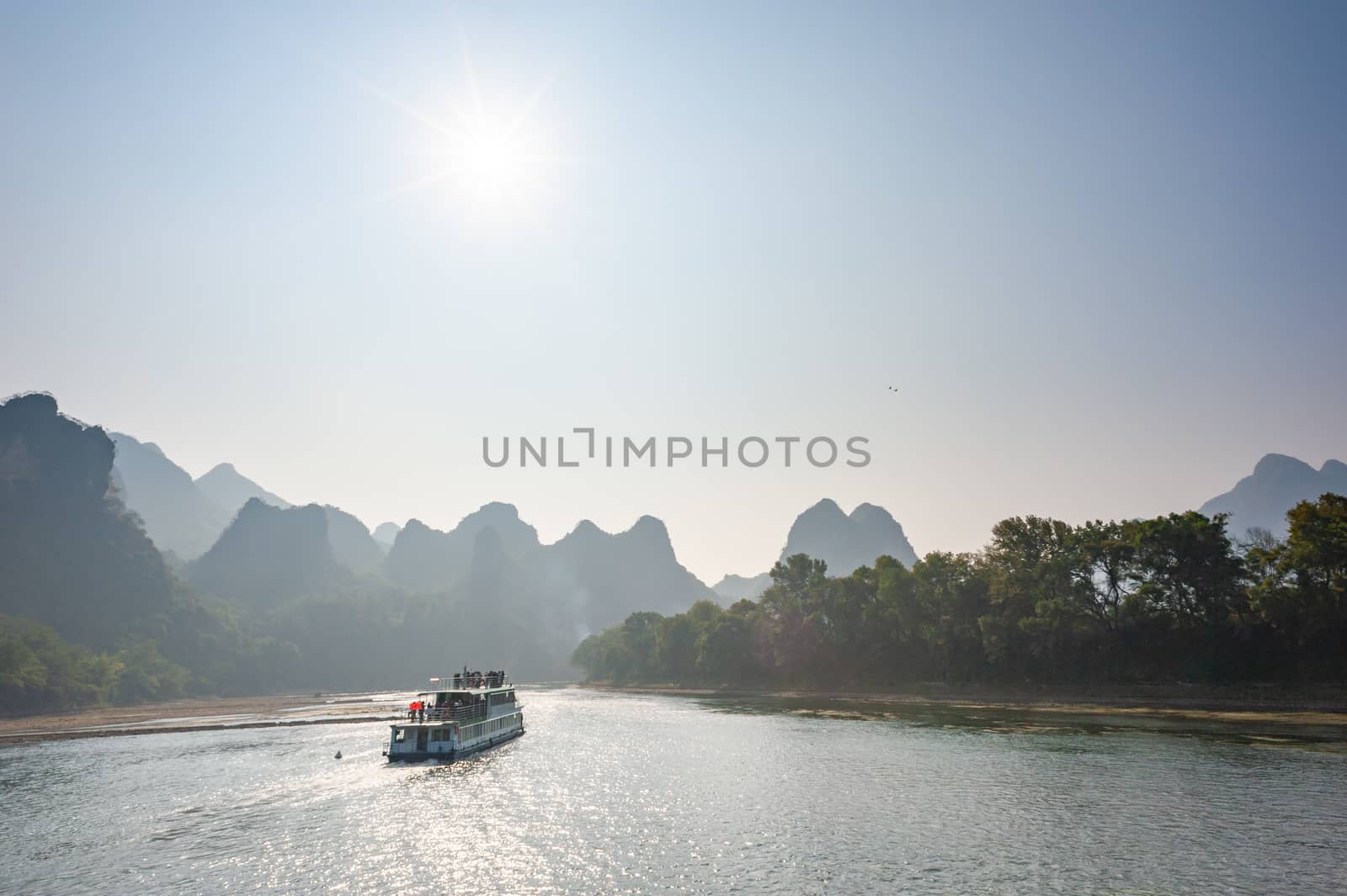 Boat on Li river cruise against the sun and karst formation mountain landscape in the fog between Guiling and Yangshuo, Guangxi province, China