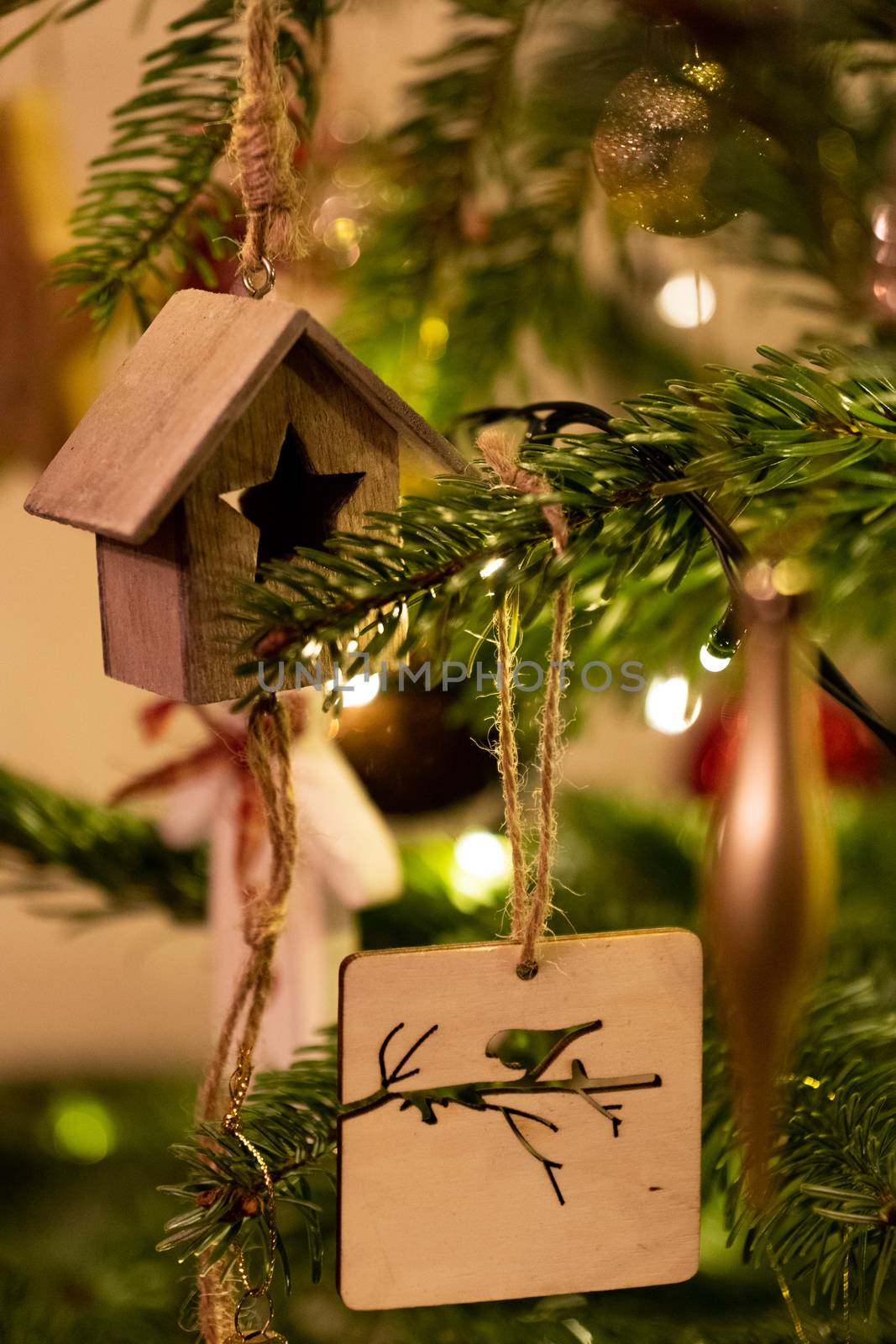 A wooden house shaped Christmas Tree Decoration hanging from a tree