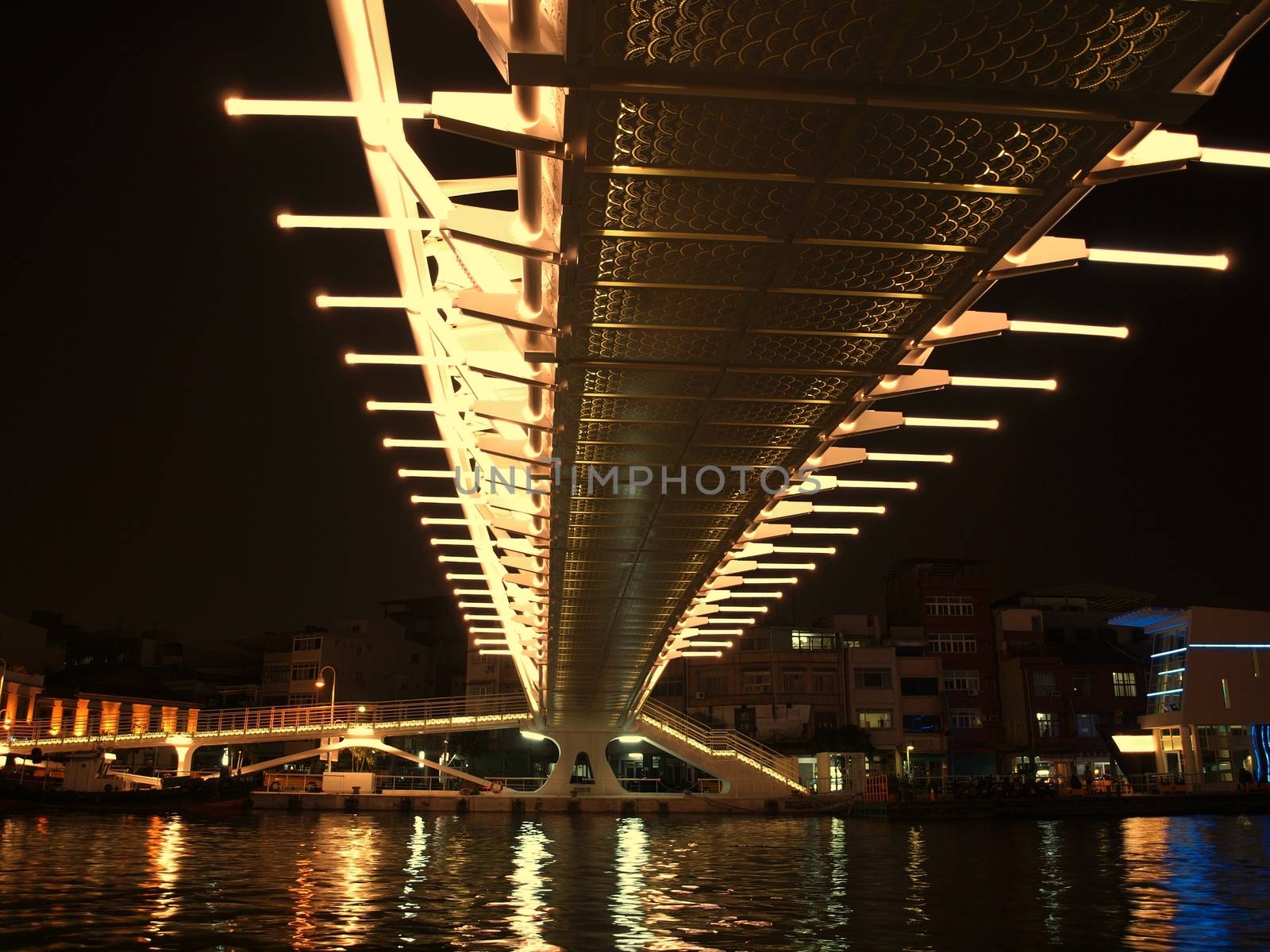 A pedestrian and bicycle bridge that spans a river, is illuminated at night
