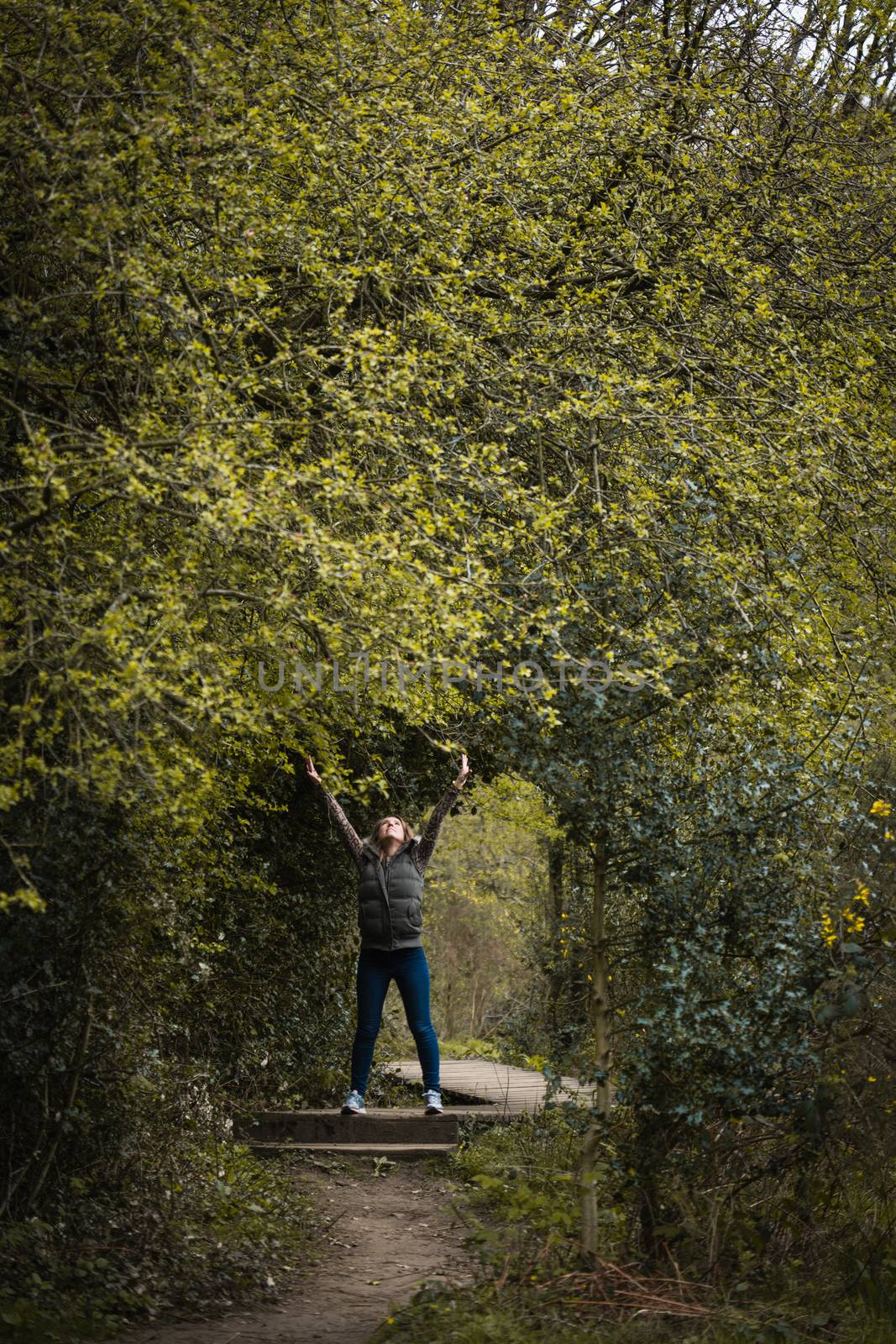 A young woman stood underneath an archway created by trees in the countryside