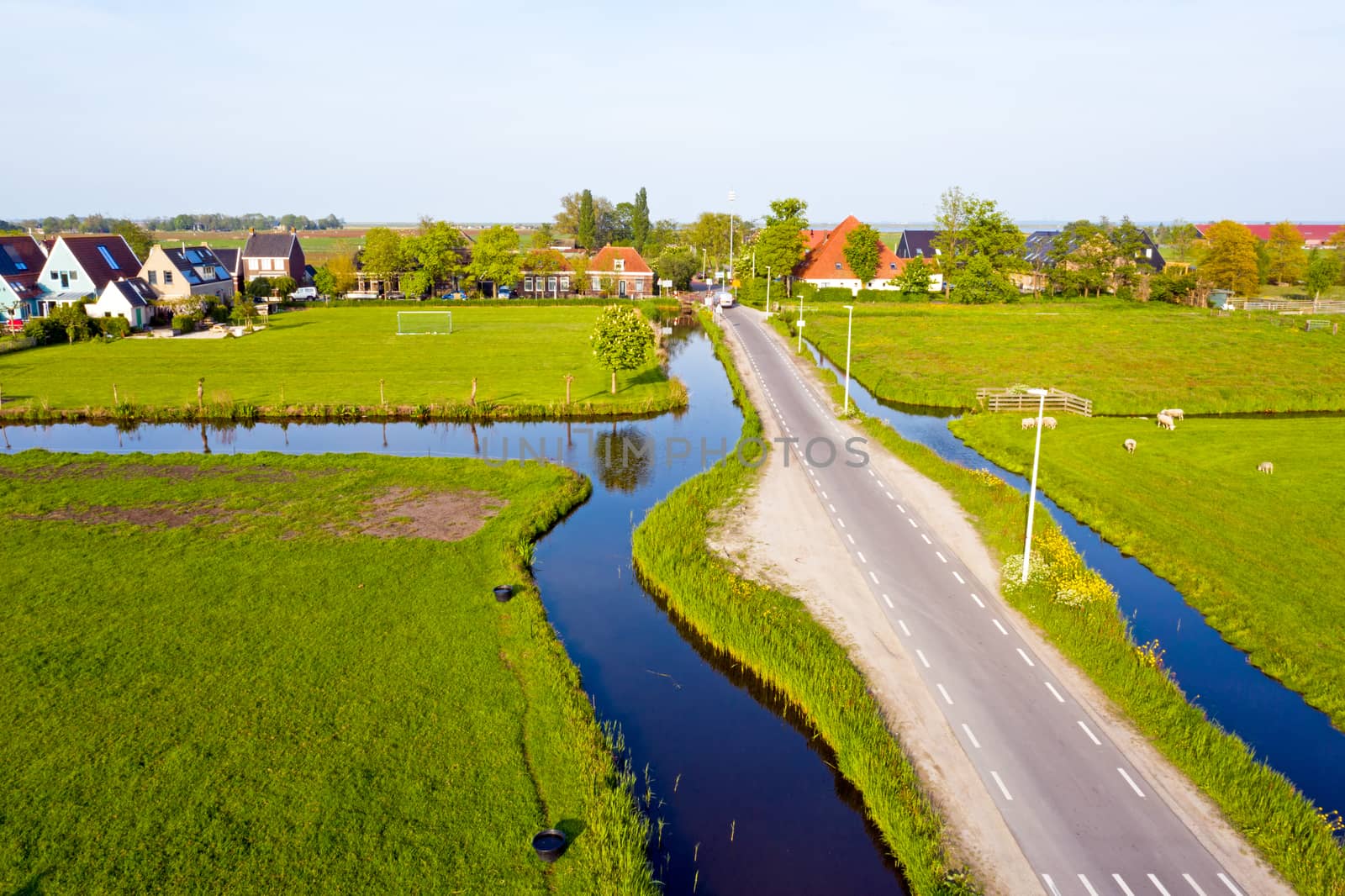 Aerial from a typical dutch landscape: flat meadows, canals and traditional wooden houses in the countryside from the Netherlands