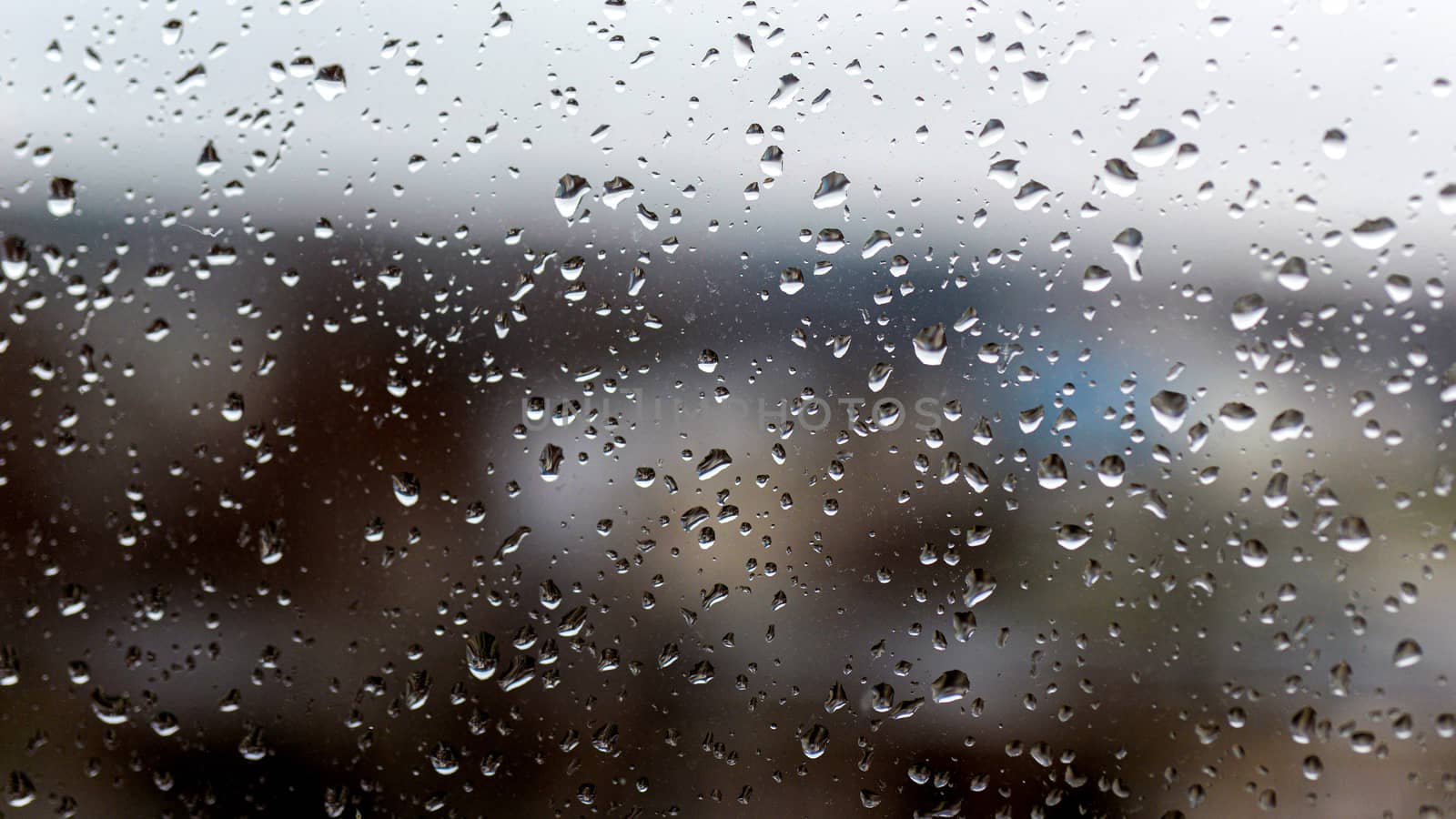 View of the city in a rainy day through a window covered with water drops - image