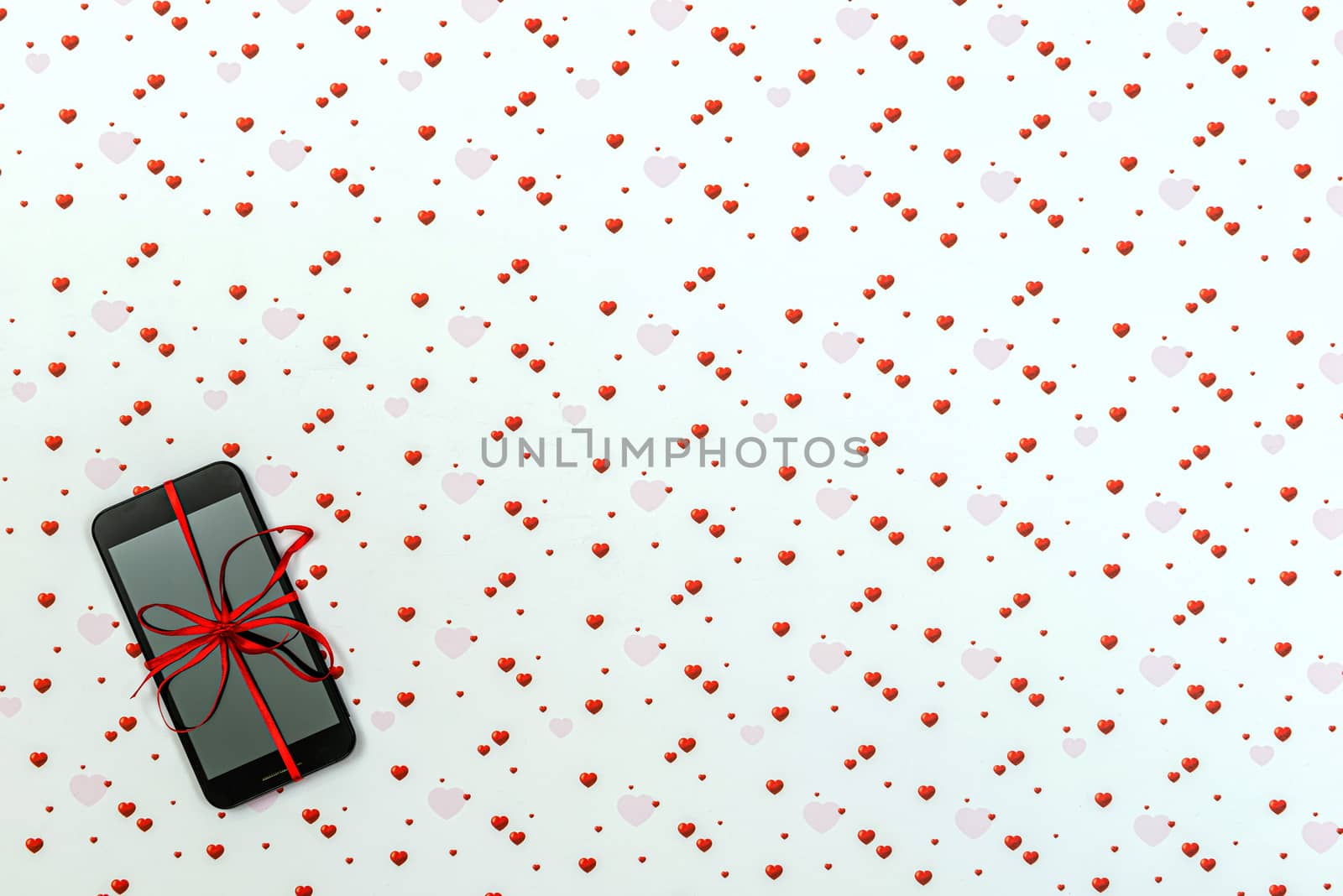 Smartphone with blank screen and red ribbon on a white bacground with colorful hearts shapes. Concept of Valentines day, birgtday, Christmas gift