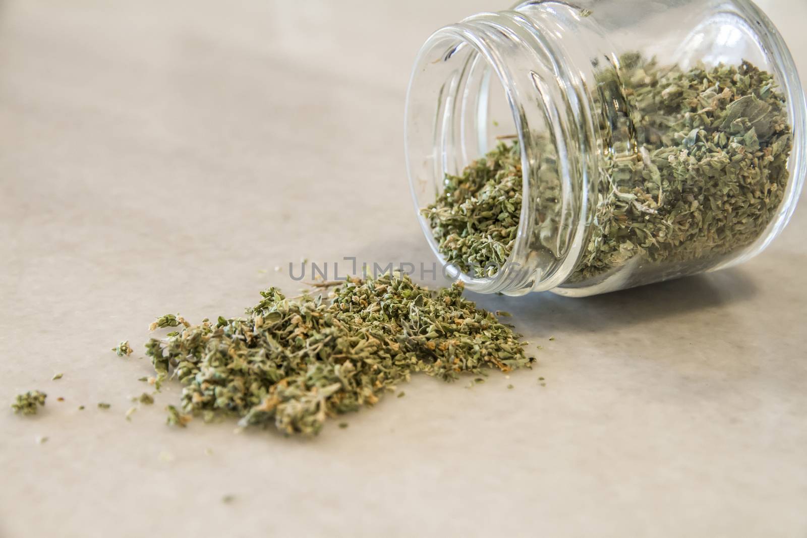 Small jar of dried oregano spilled on a marble top with selective focus