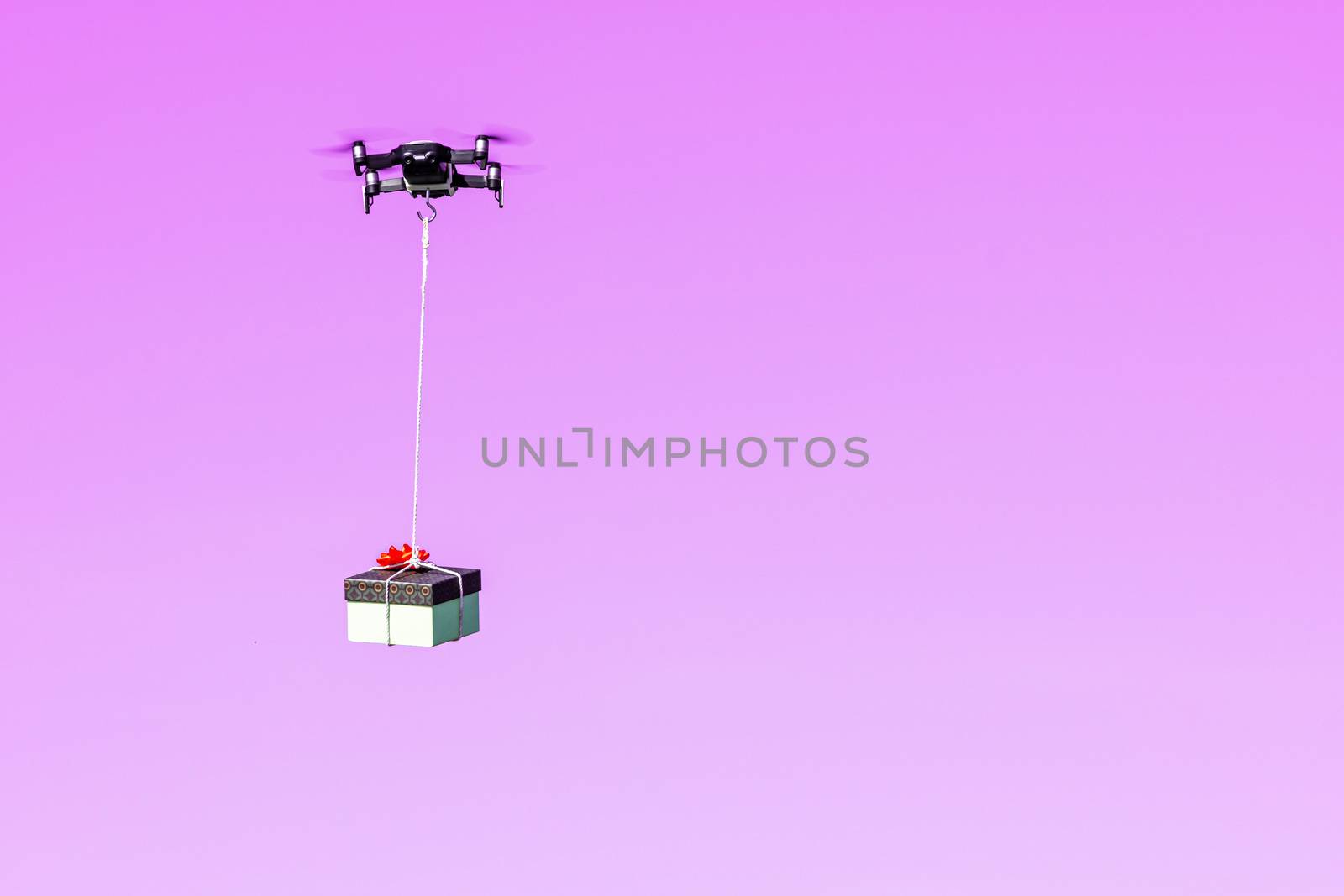 multicopter drone flying with a gift box isolated on a pink background, concept of modern fast delivery method by using drones