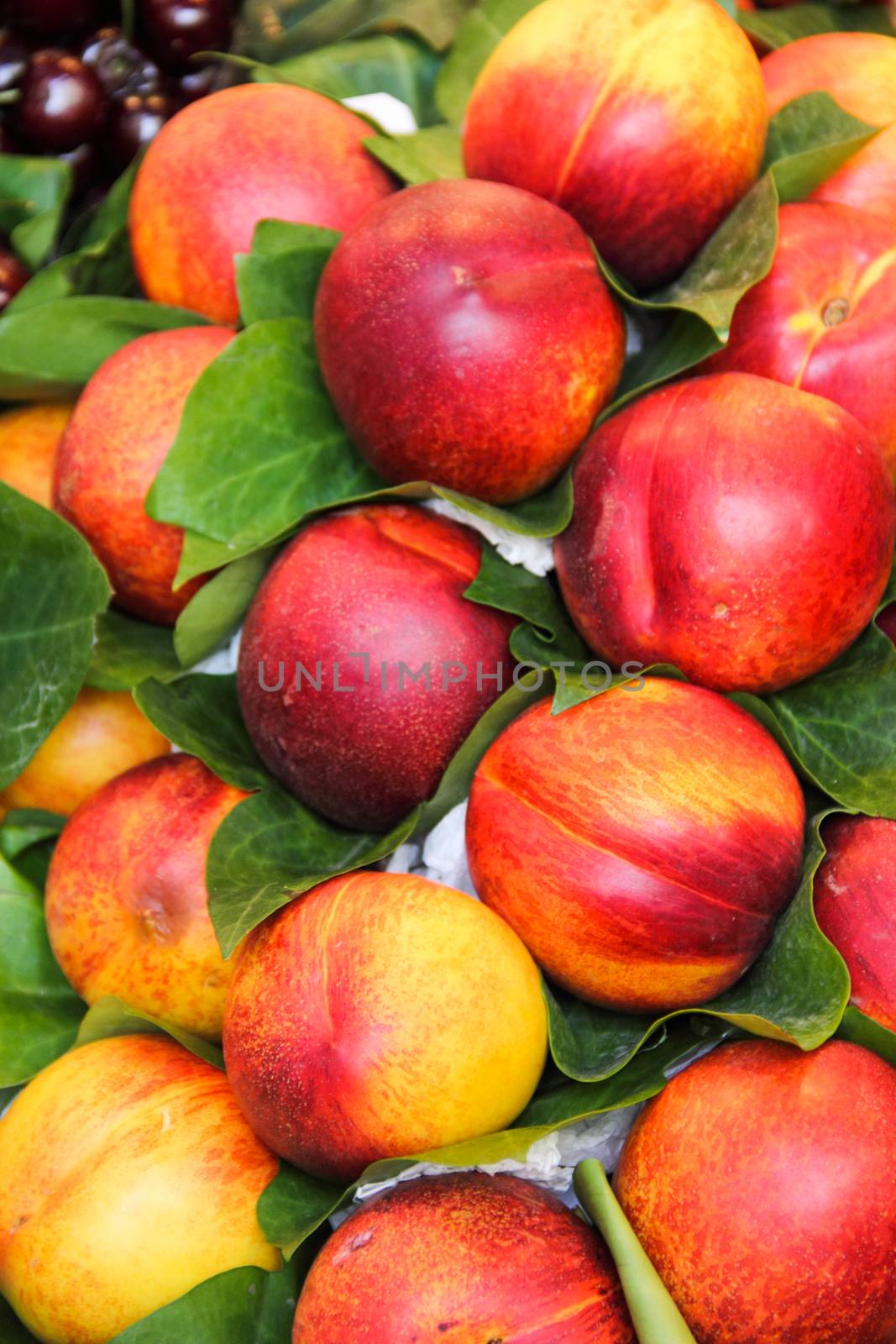 Lot of red fresh nectarine fruits with leaves at market, food background