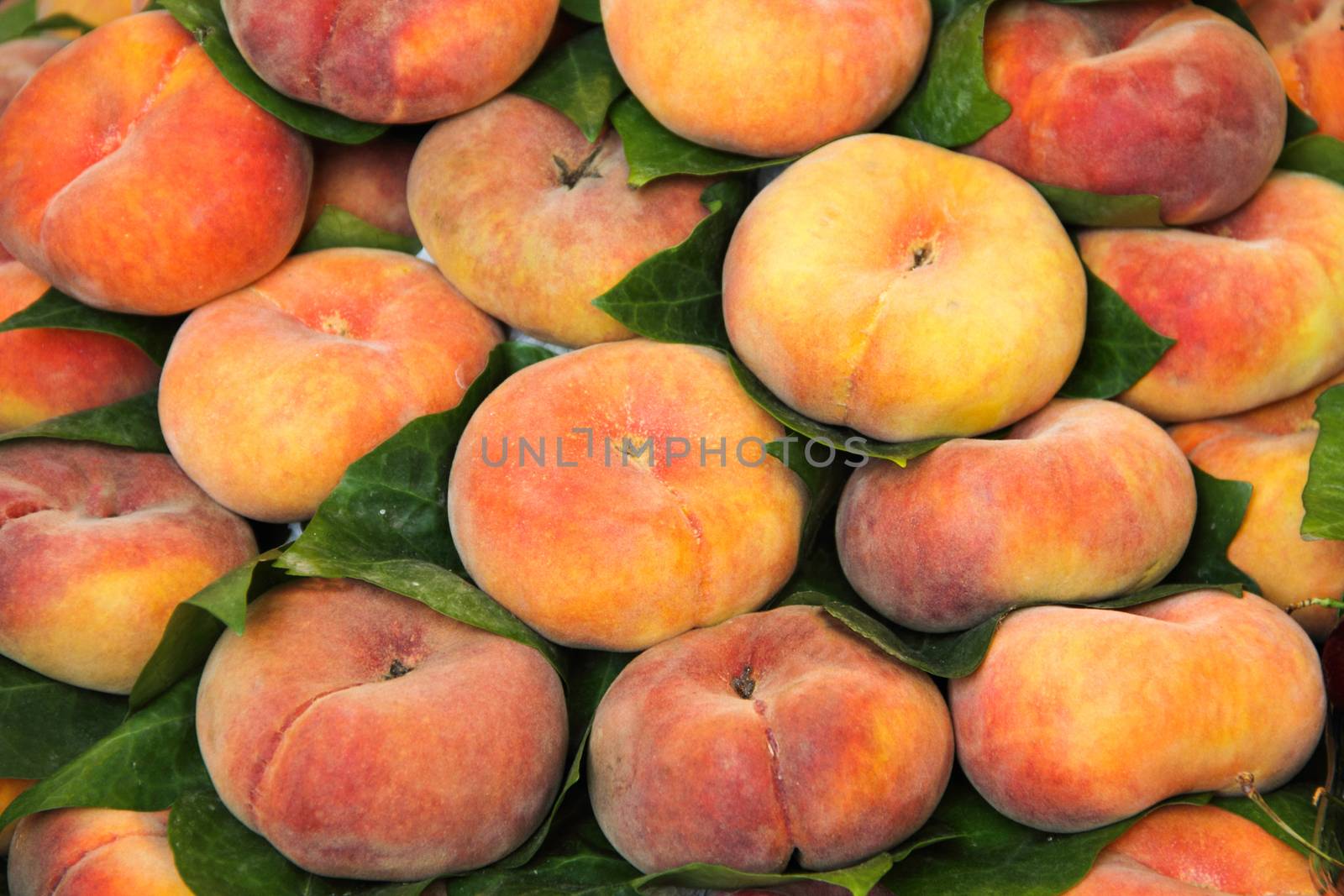 Lot of red fresh peach fruits with leaves at market, food background