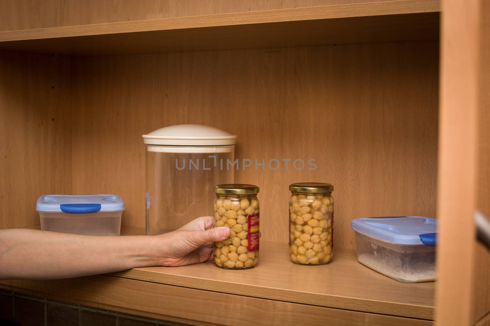 woman picking up a pot of chickpeas from the kitchen pantry