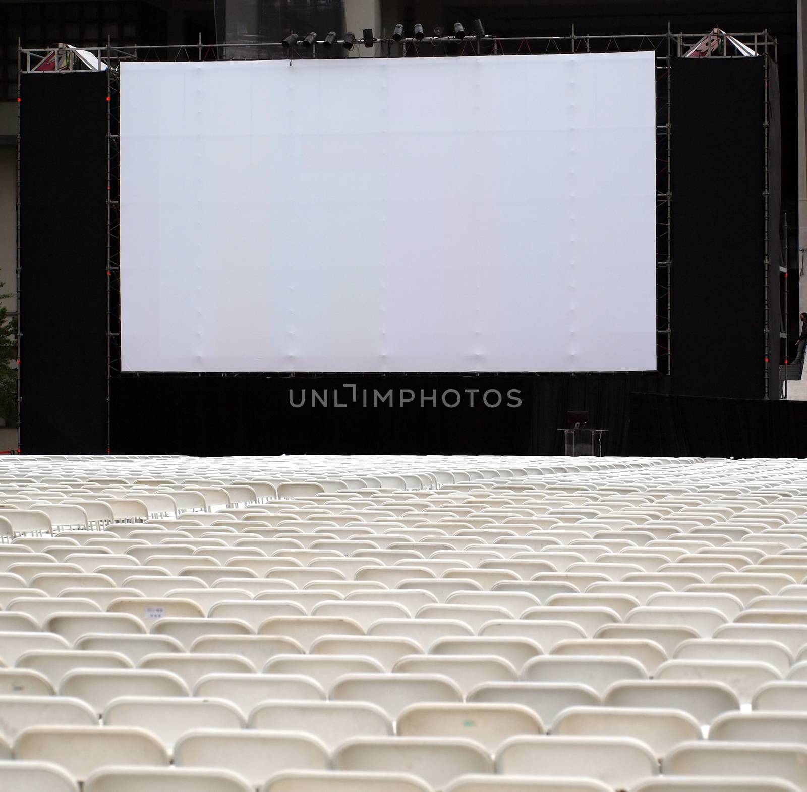 Rows of white plastic chairs are set up for an outdoor movie show

