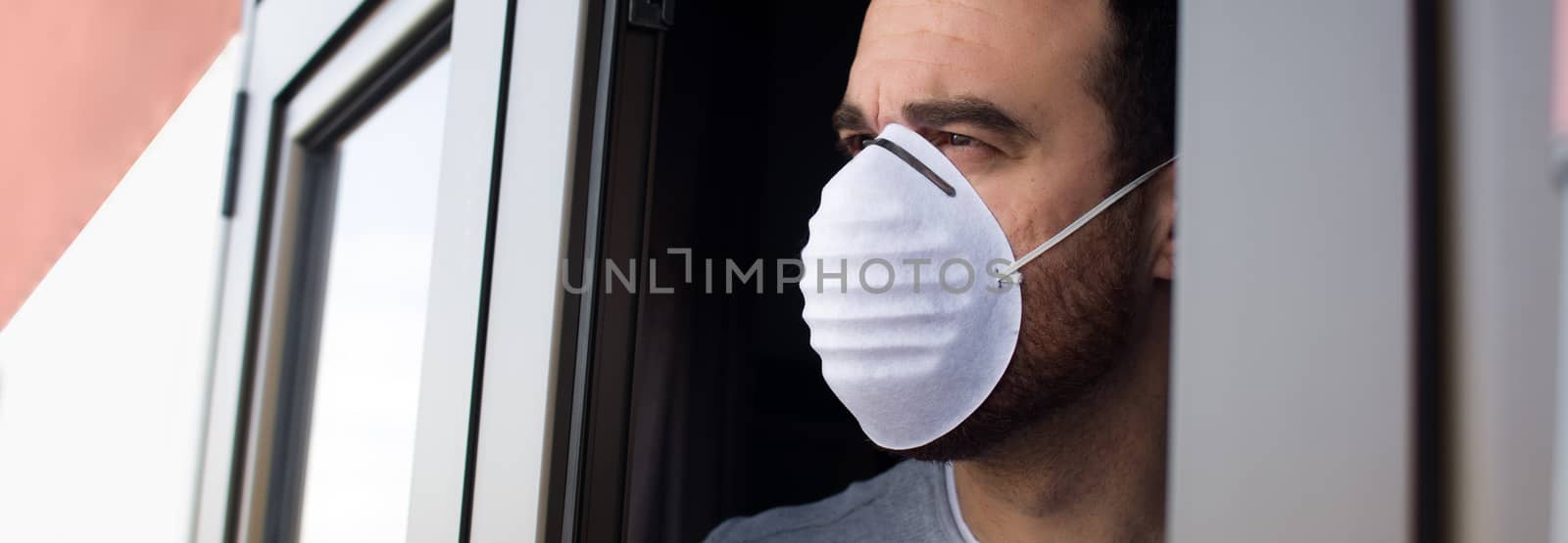 Man with face mask and gloves looking out the window. Stay at home concept. Panorama photo.