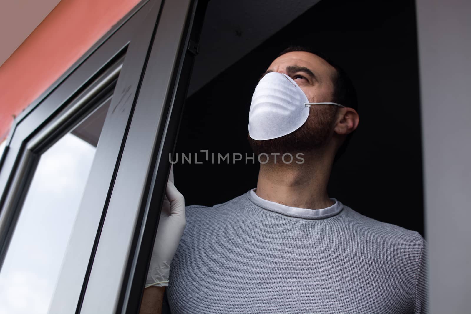 Man with face mask and gloves looking out the window by chandlervid85