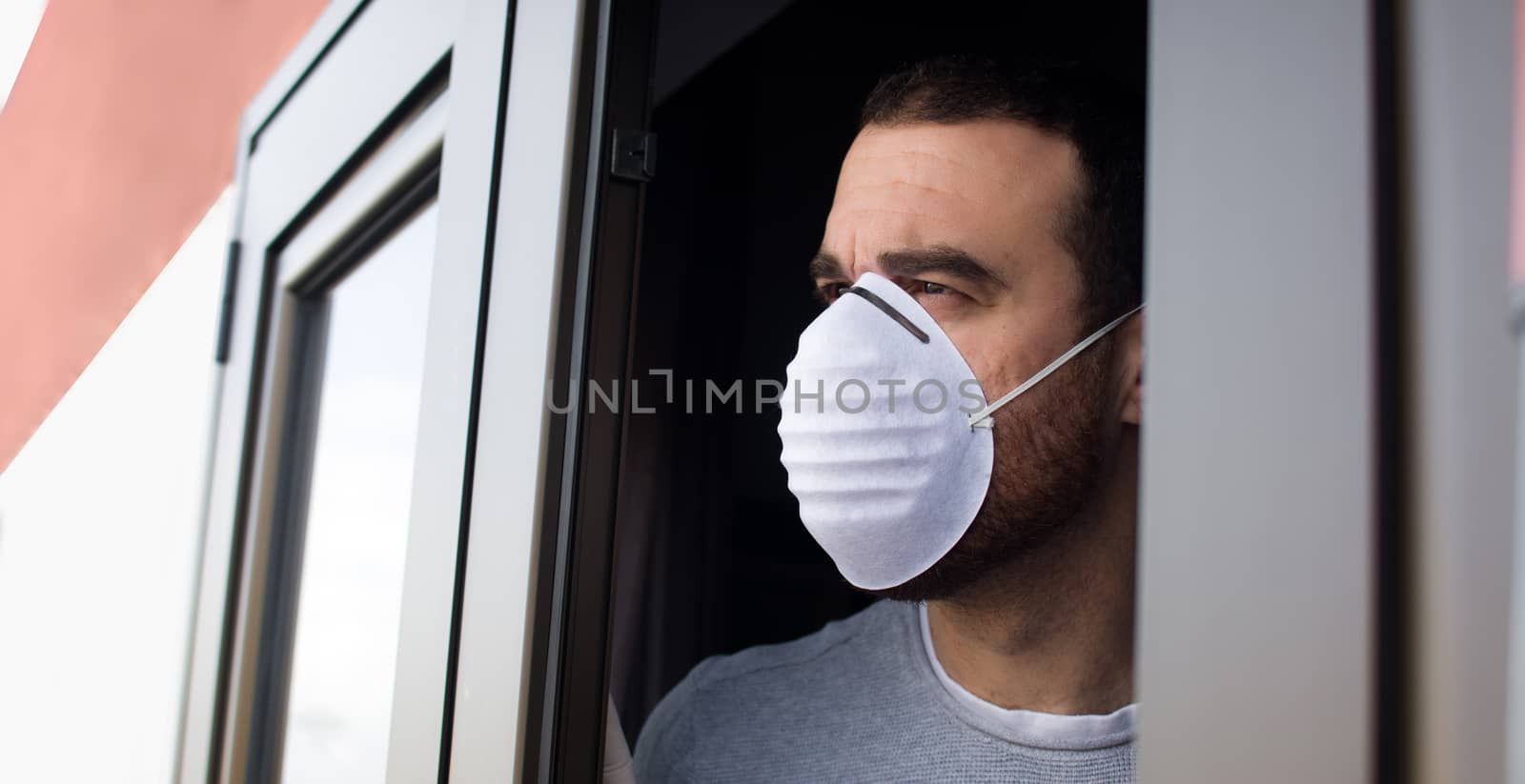 Man with face mask and gloves looking out the window by chandlervid85