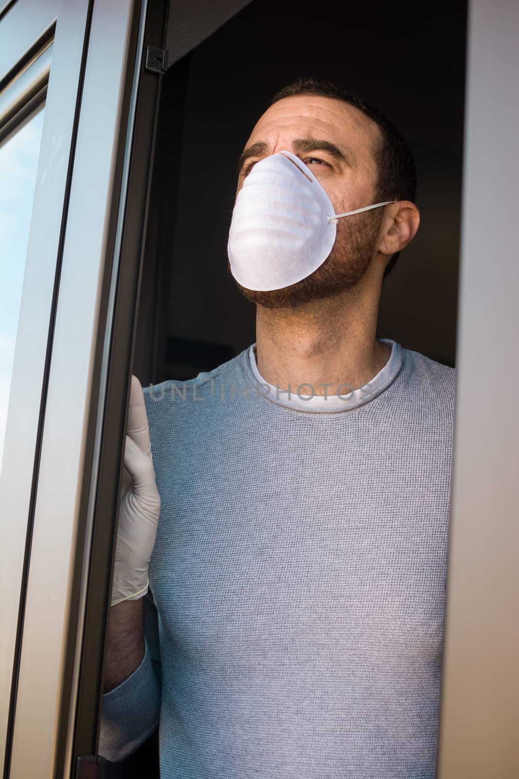 Man with face mask and gloves looking out the window