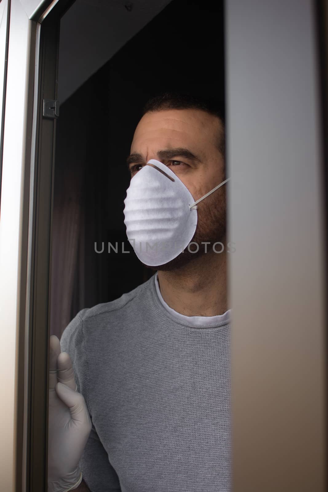 Man with face mask and gloves looking out the window by chandlervid85