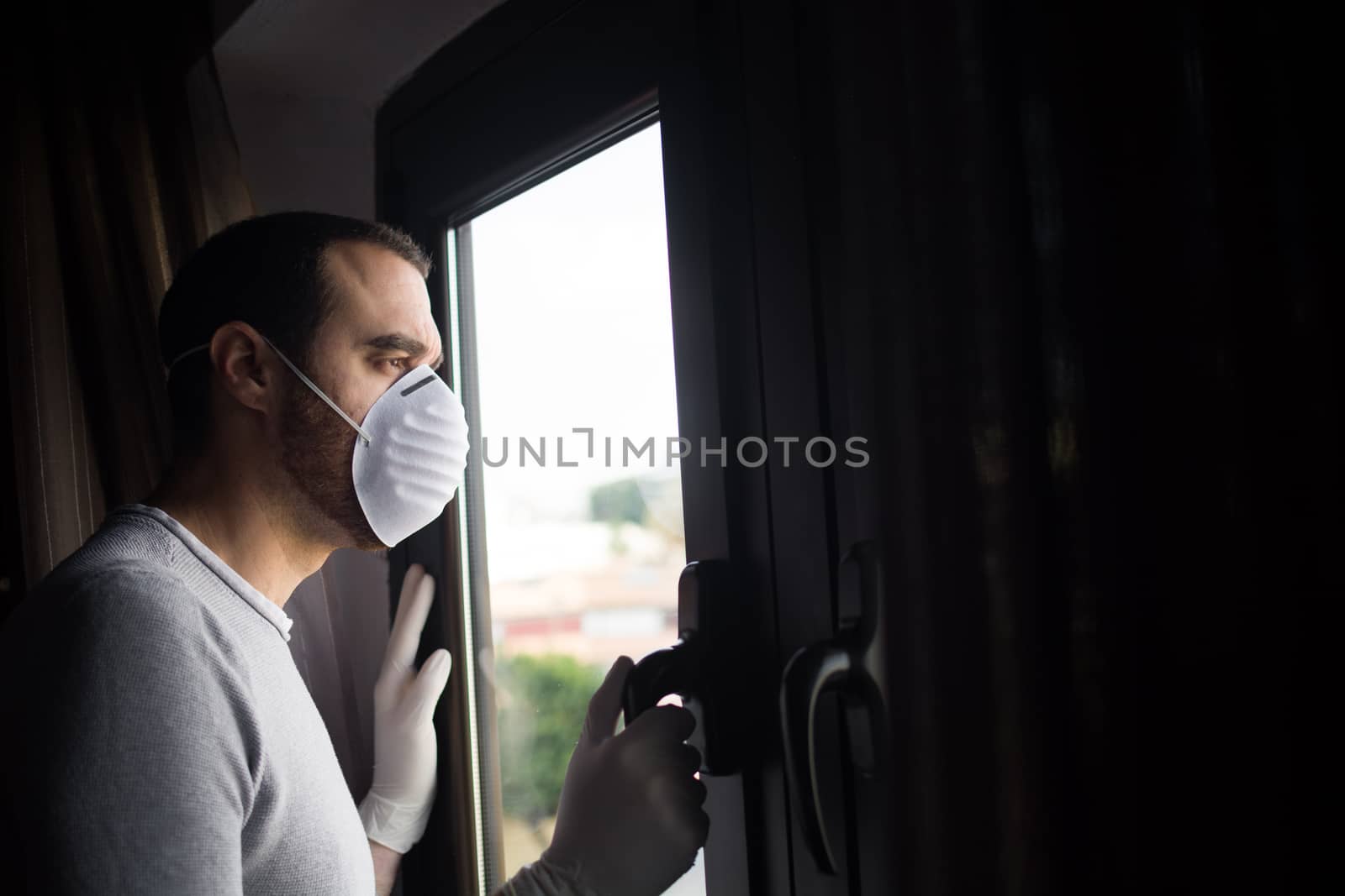Man with face mask and gloves looking out the window by chandlervid85