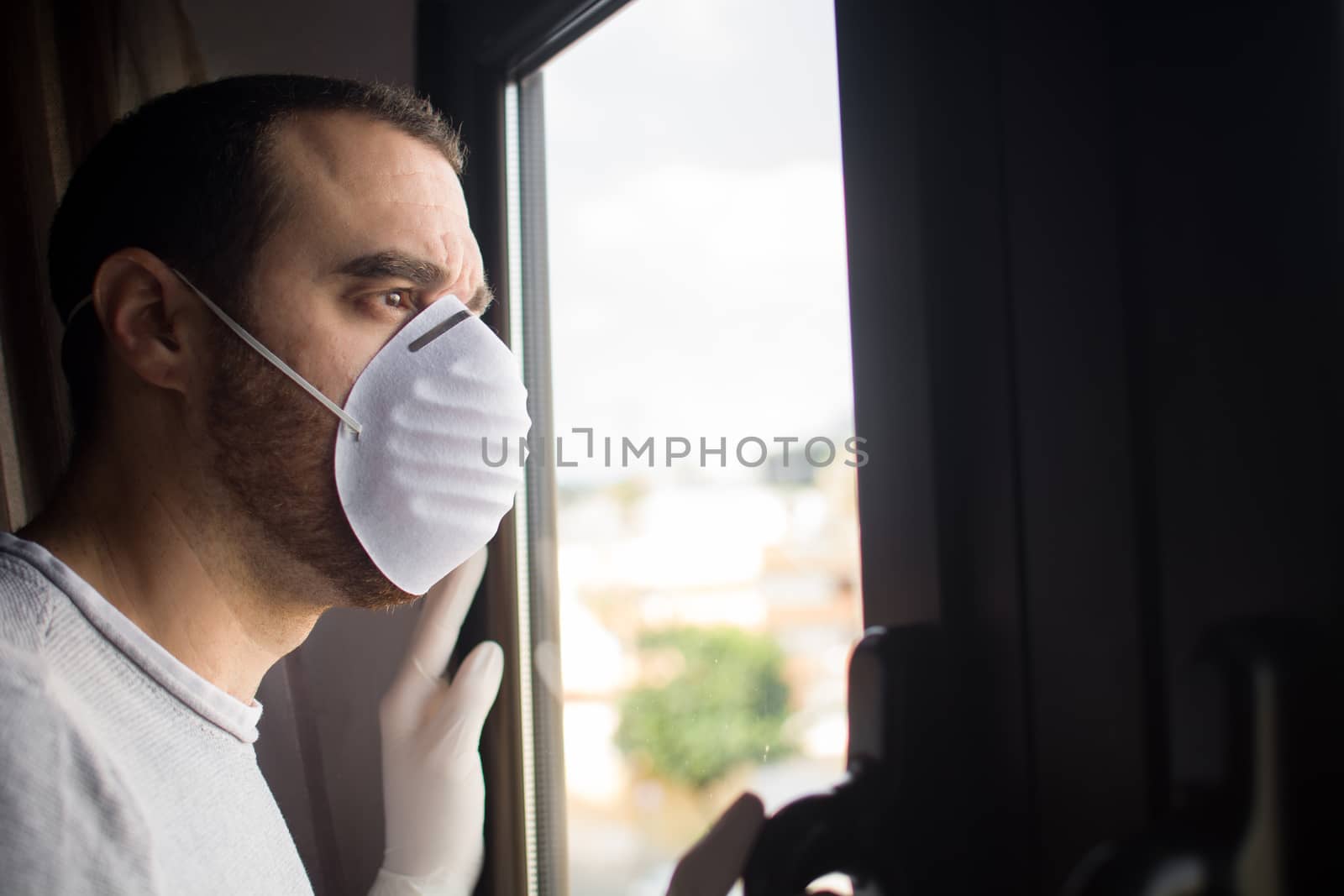 Man with face mask and gloves looking out the window by chandlervid85