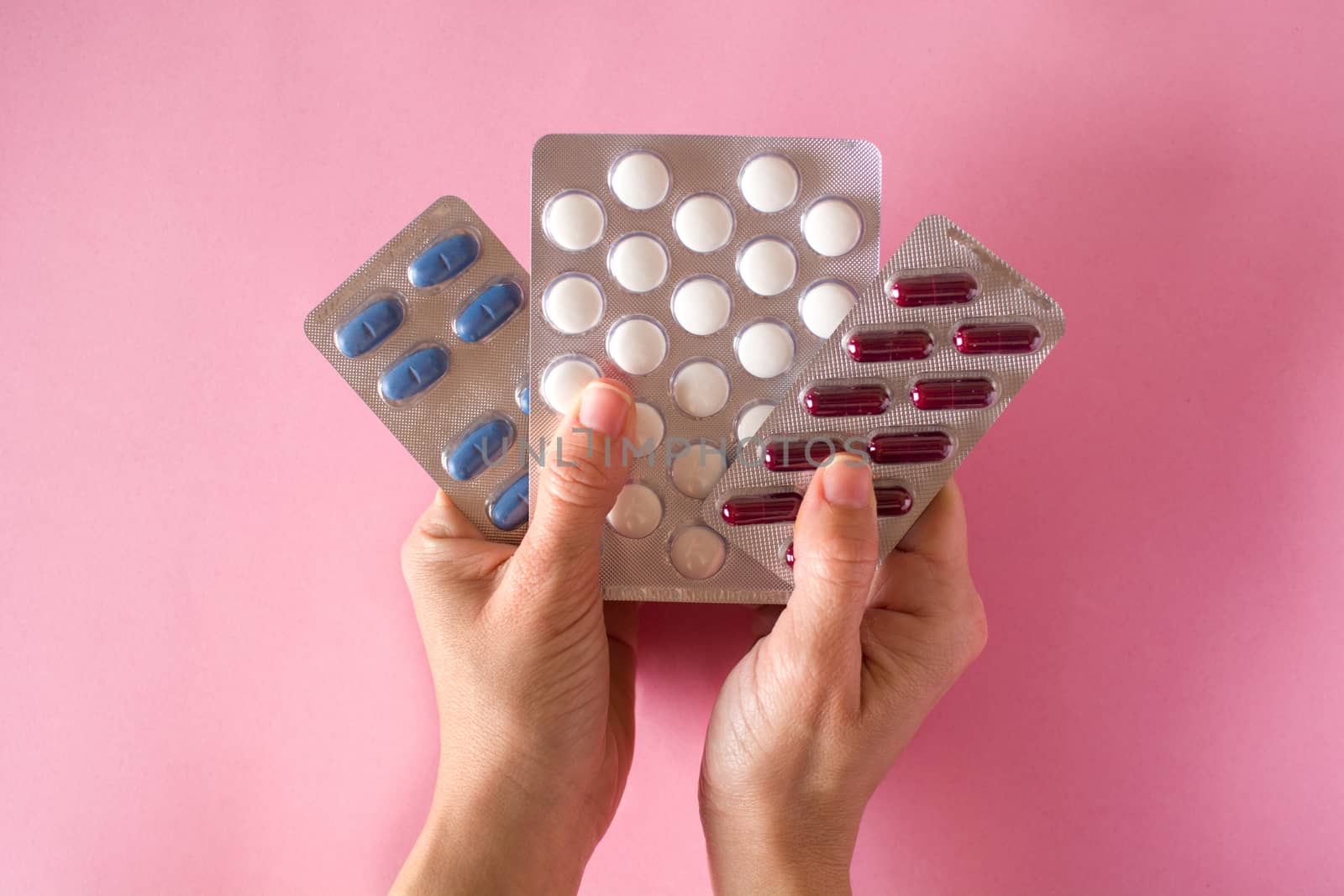 Female hand holding medical pills on pink background