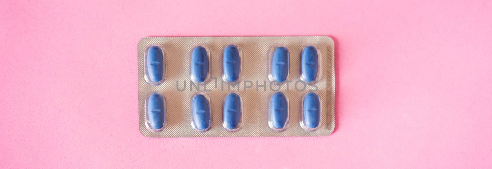 Blue medical pills on pink background. Panorama photo.