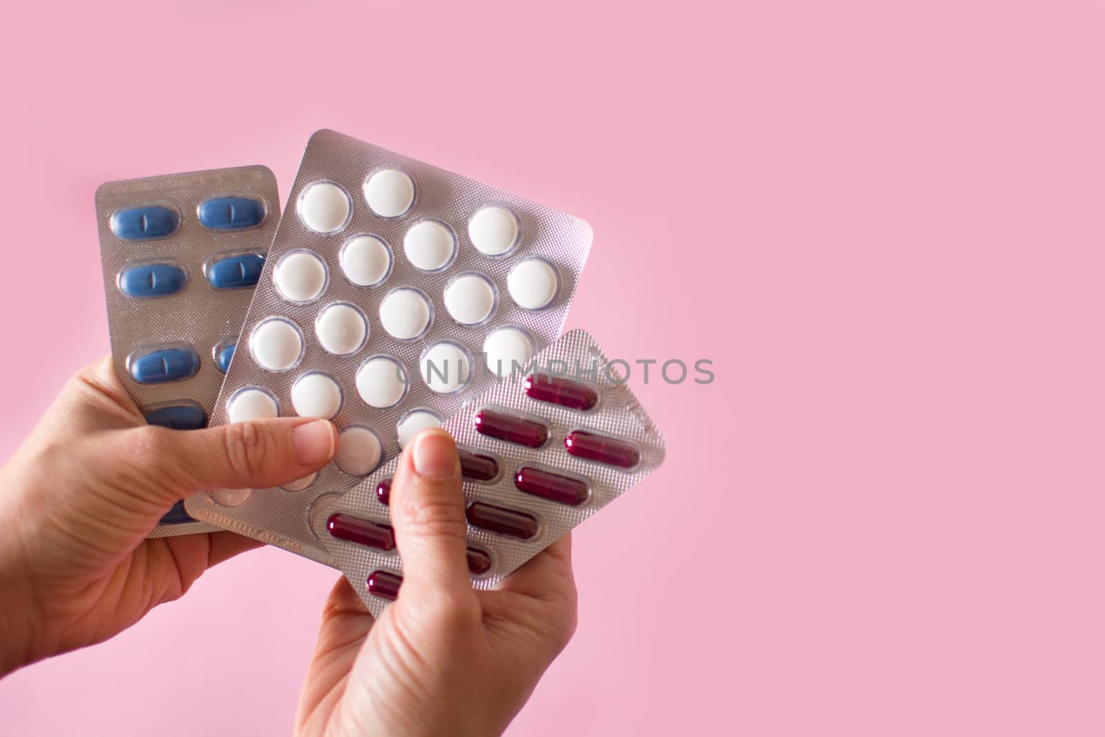 Female hand holding medical pills on pink background copy space by chandlervid85