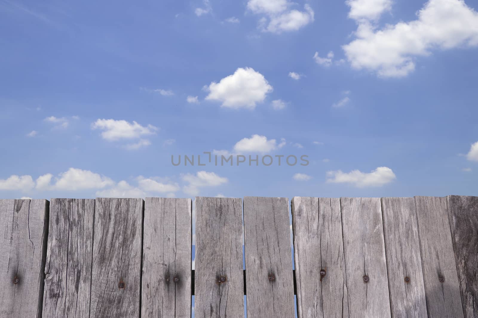 Old wooden fence with bright sky and clouds.