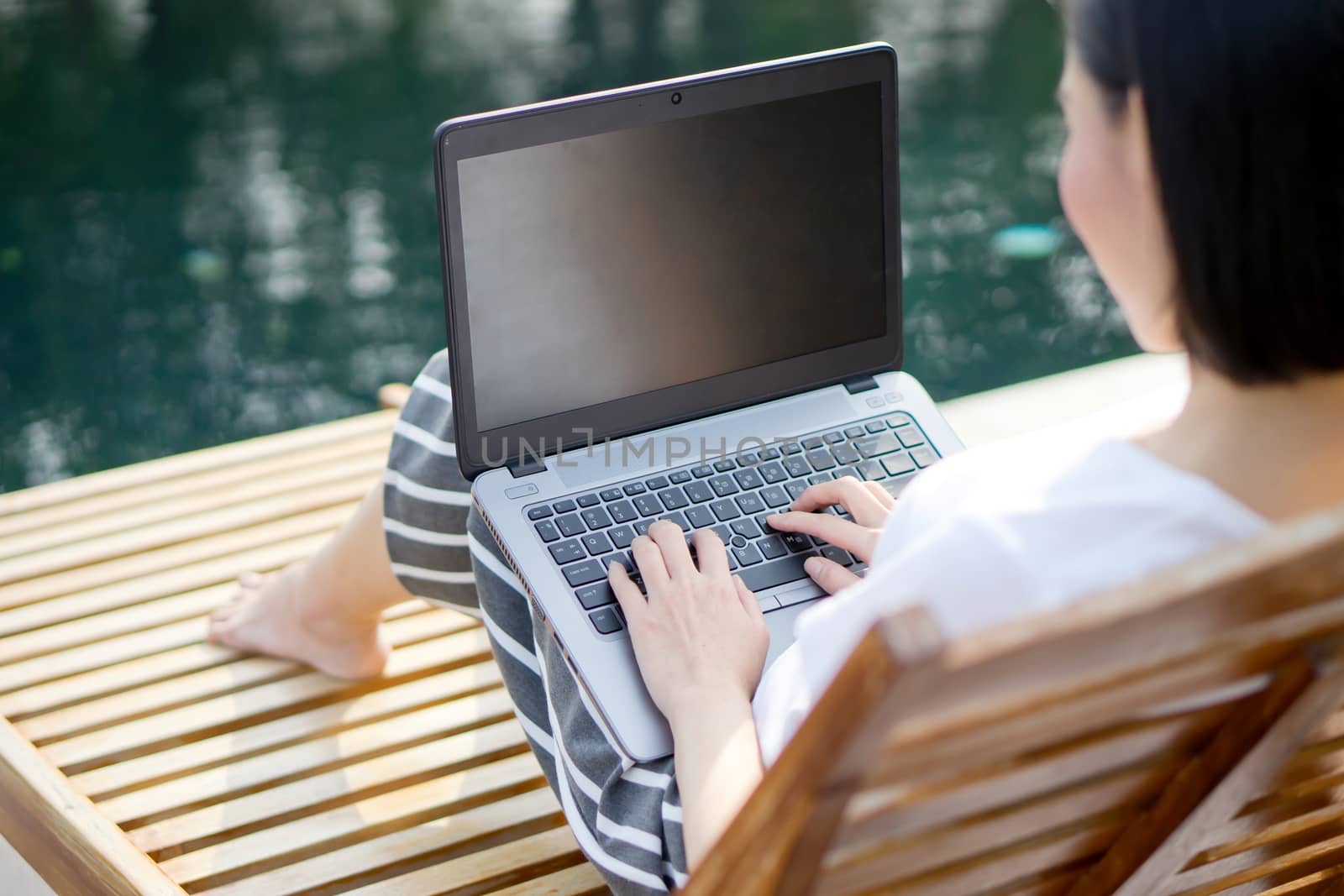 Woman working with laptop computer sitting at swimming pool