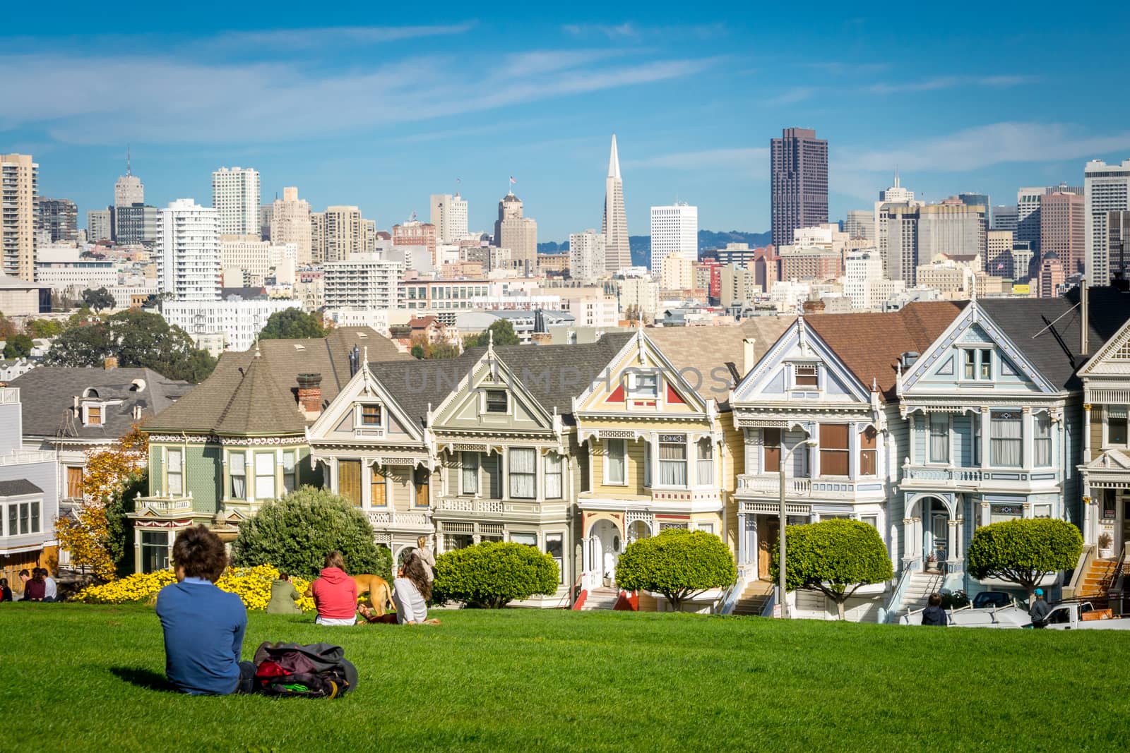 San Francisco, California, United States, November 2013: View on the Painted Ladies Victorian houses of San Francisco with cityscape and skyline in the background on a blue sky. People sitting front