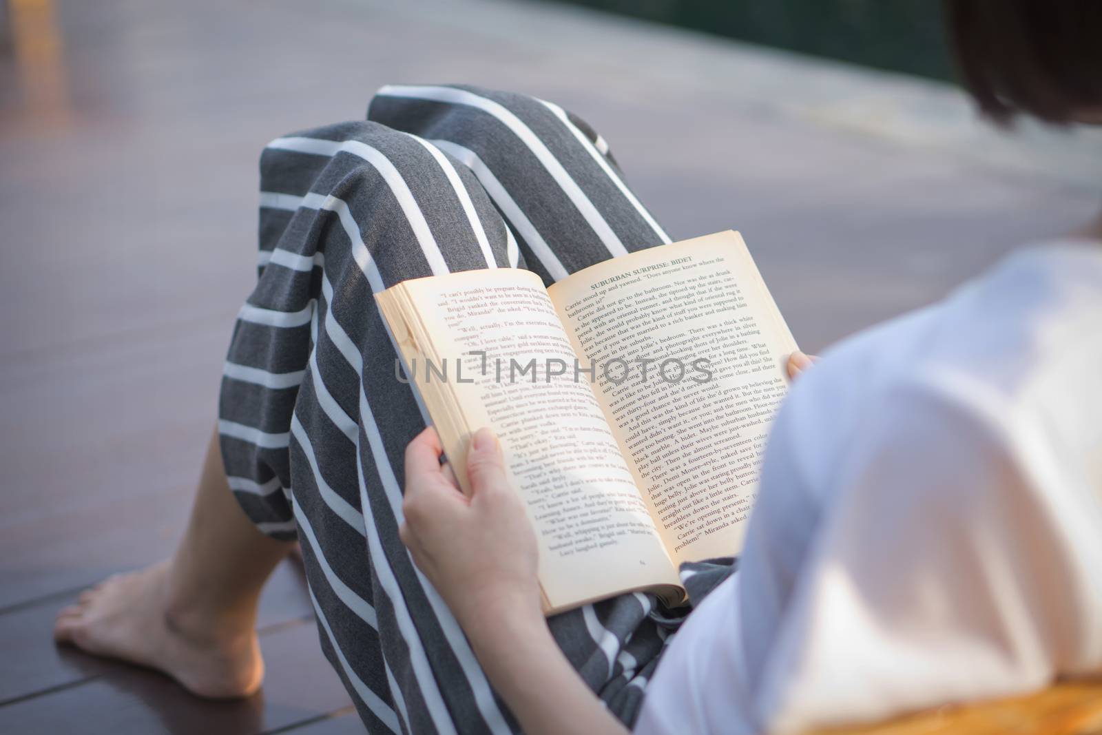 Beautiful young woman reading book on sun lounger by swimming pool