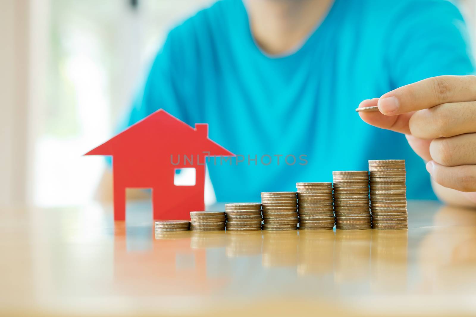 Human hand add a  coin in the final row of  coins over red  house  