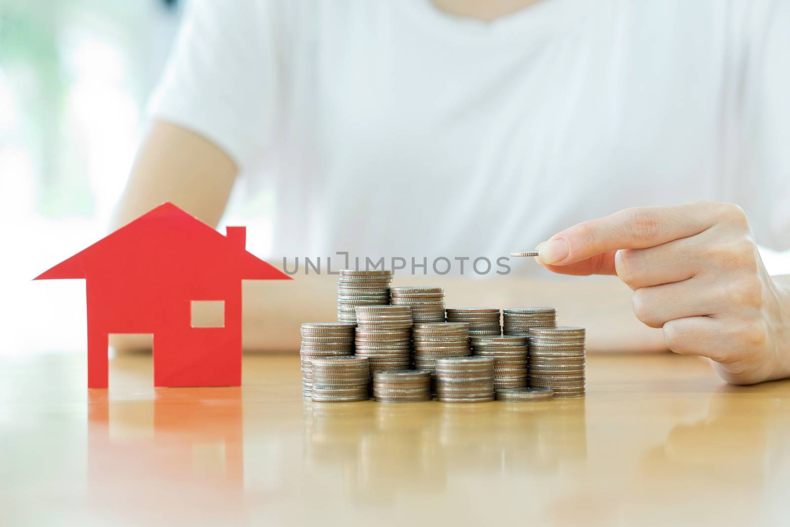 woman put coins to stack of coins and red house blackground