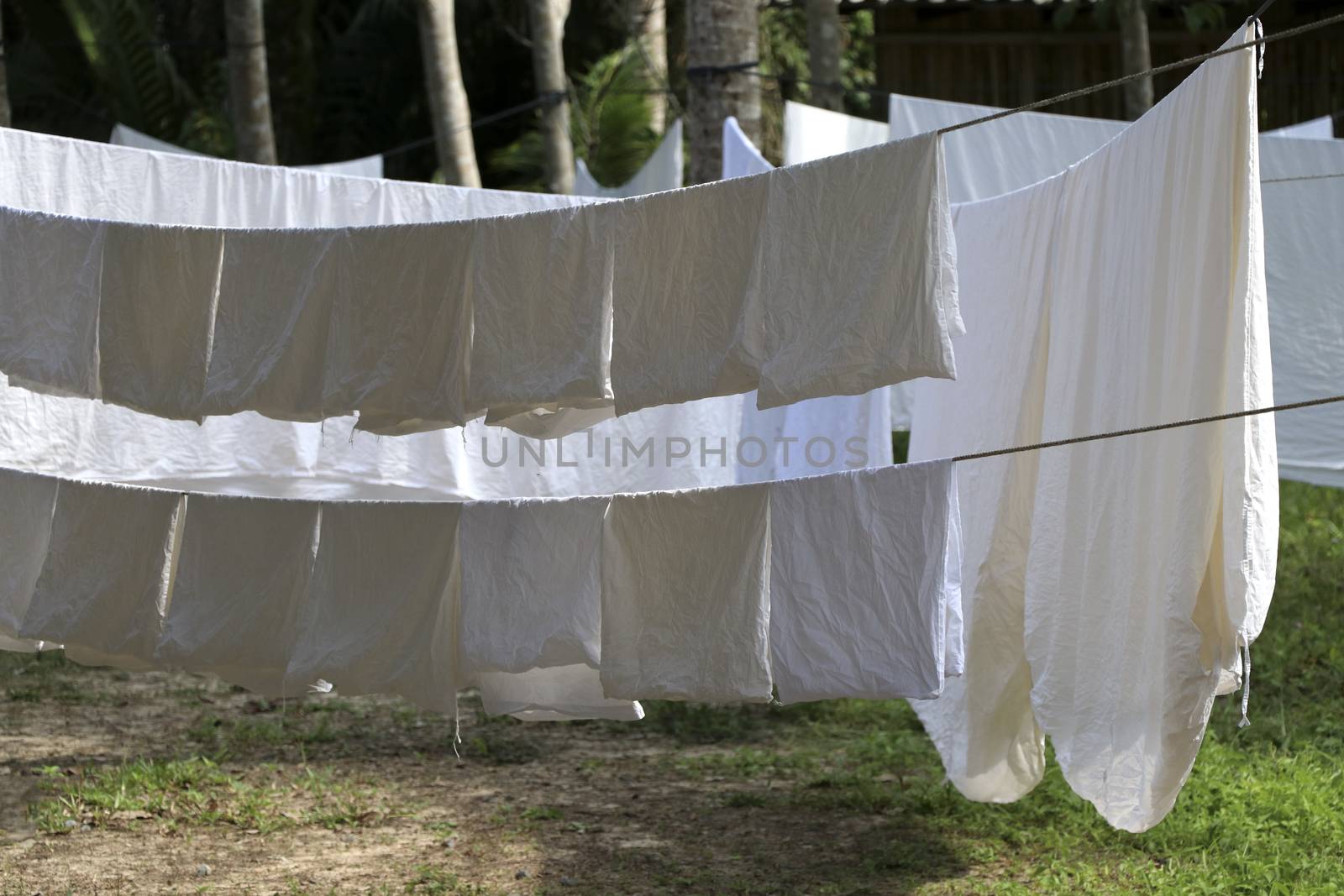 The white cloth is exposed to the sun on the clothesline. A large white cloth hung on a clothesline.