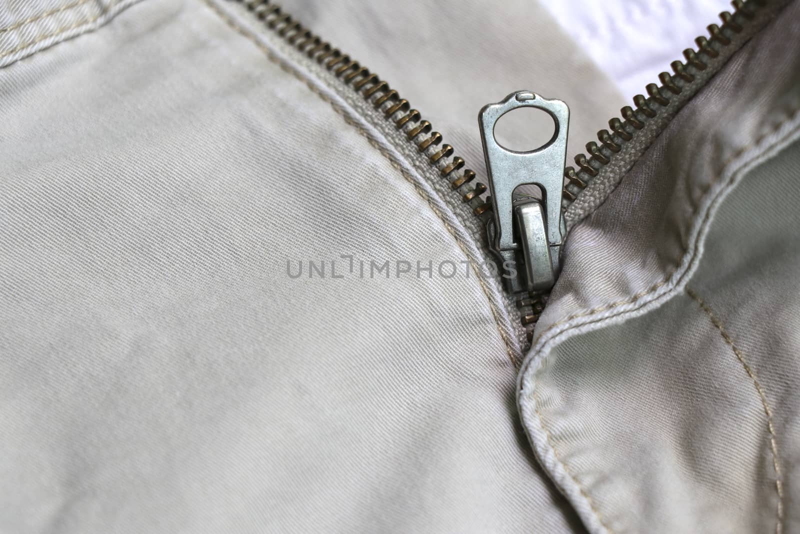 The zipper of the pants that opened. Metal zipper of cream pants.