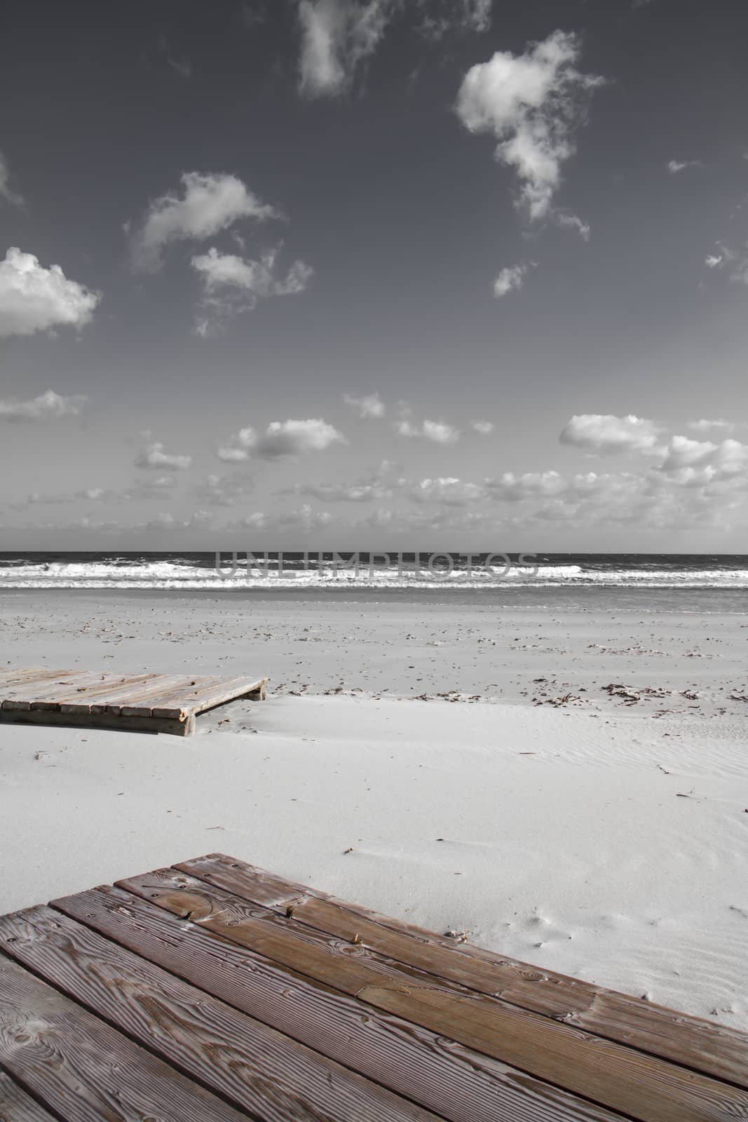 Boardwalk in the winter sea. In the solitude of the finished season the wooden platforms lie abandoned on the white sand, moved by the impetuous sea