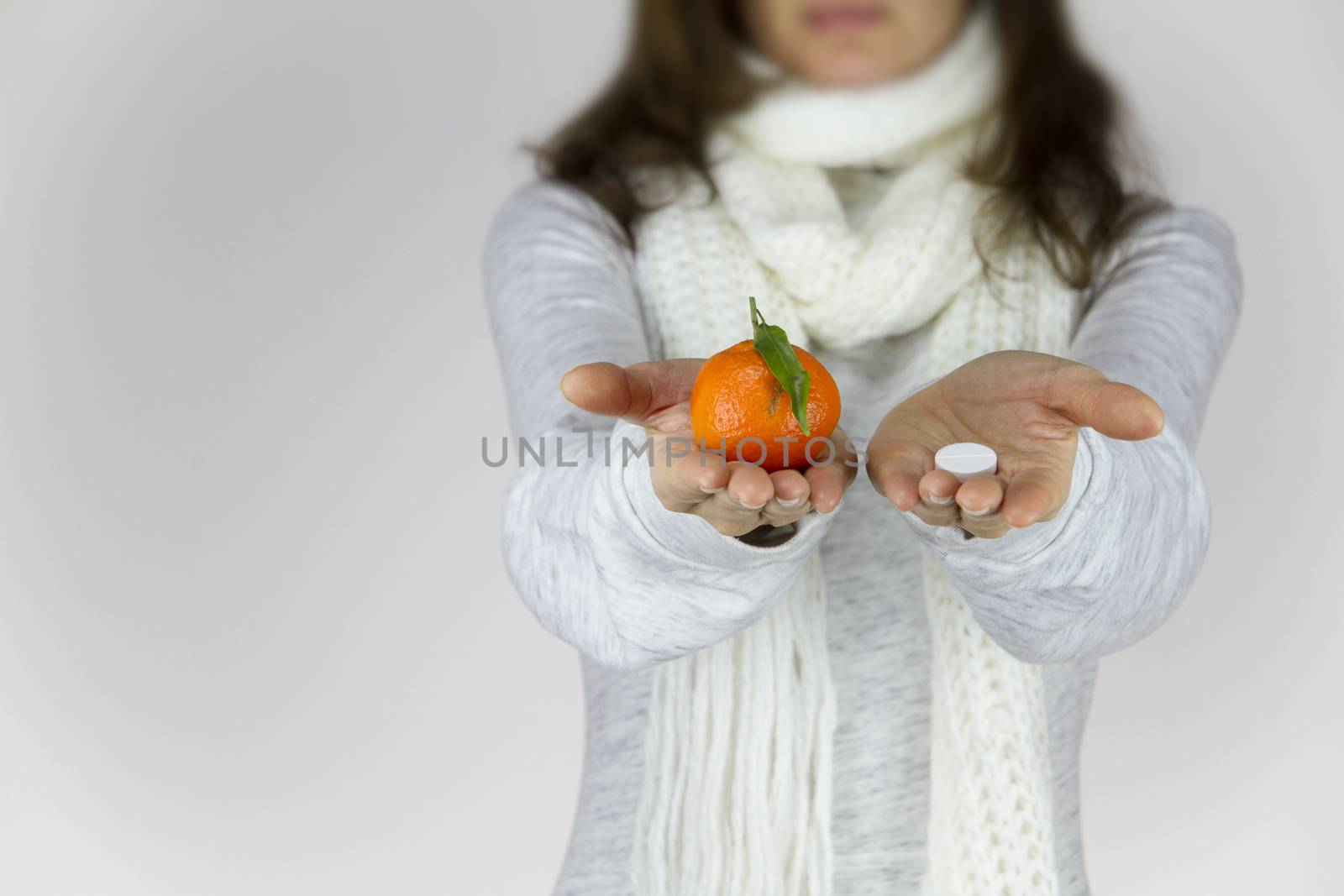 Vitamins from fruit or drugs? A sick young woman with a scarf on her neck shows a mandarin in her right hand and an aspirin on her left